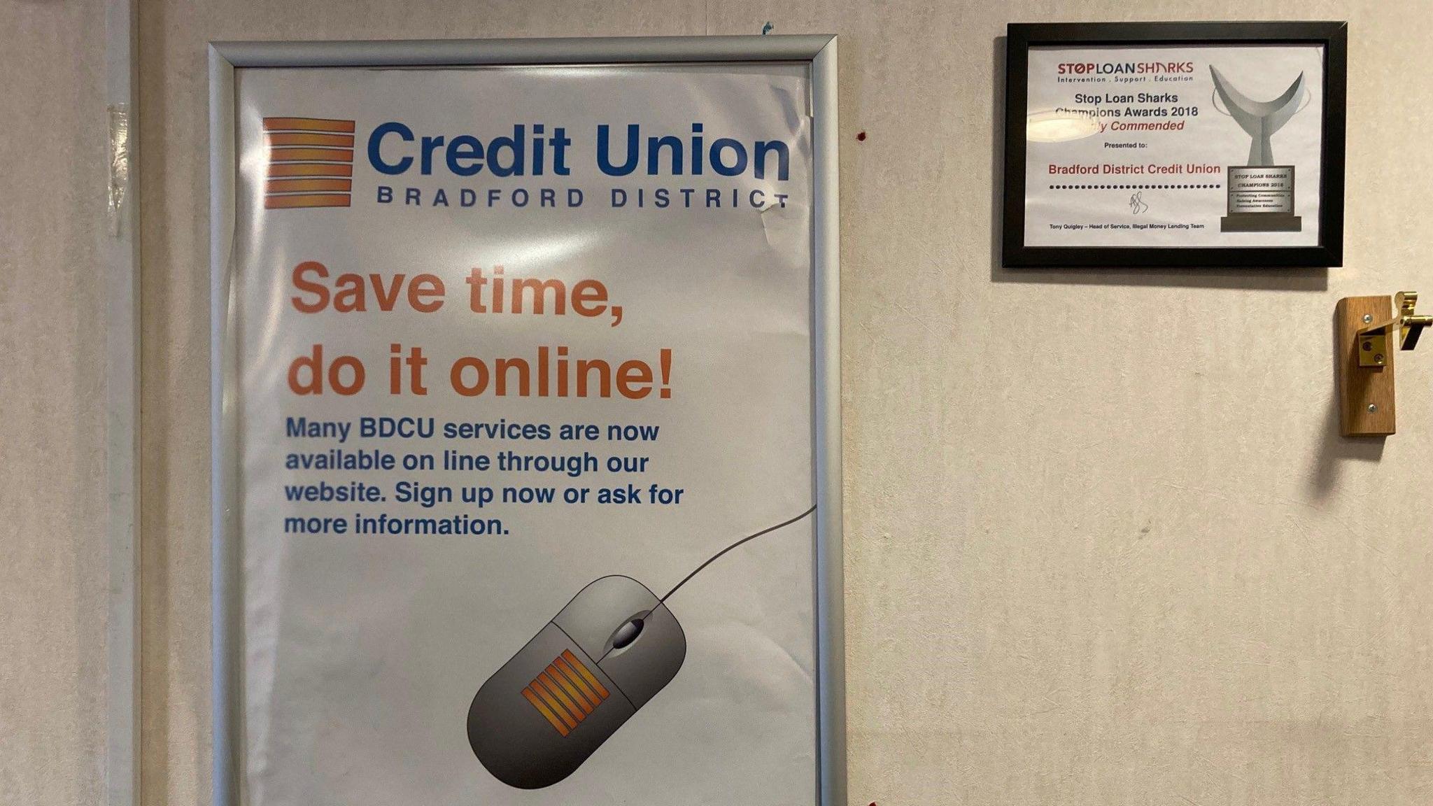 A poster for the Bradford District Credit Union with a picture of a grey computer mouse with a yellow striped design on it next to a framed certificate for the service from the Stop Loan Sharks awards.  