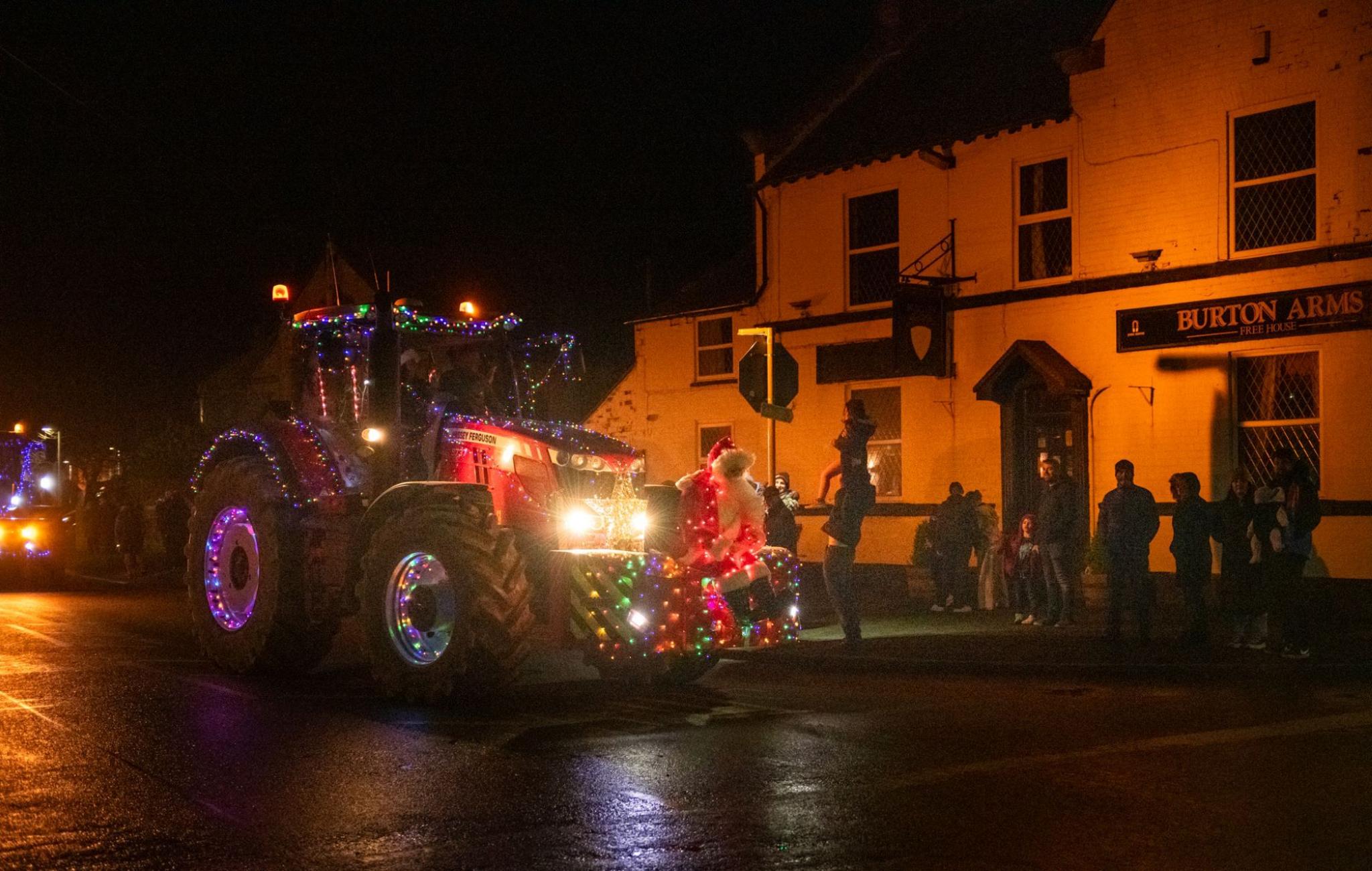 A model of Father Christmas is attached to the front of a tractor, which is decorated in Christmas lights. 