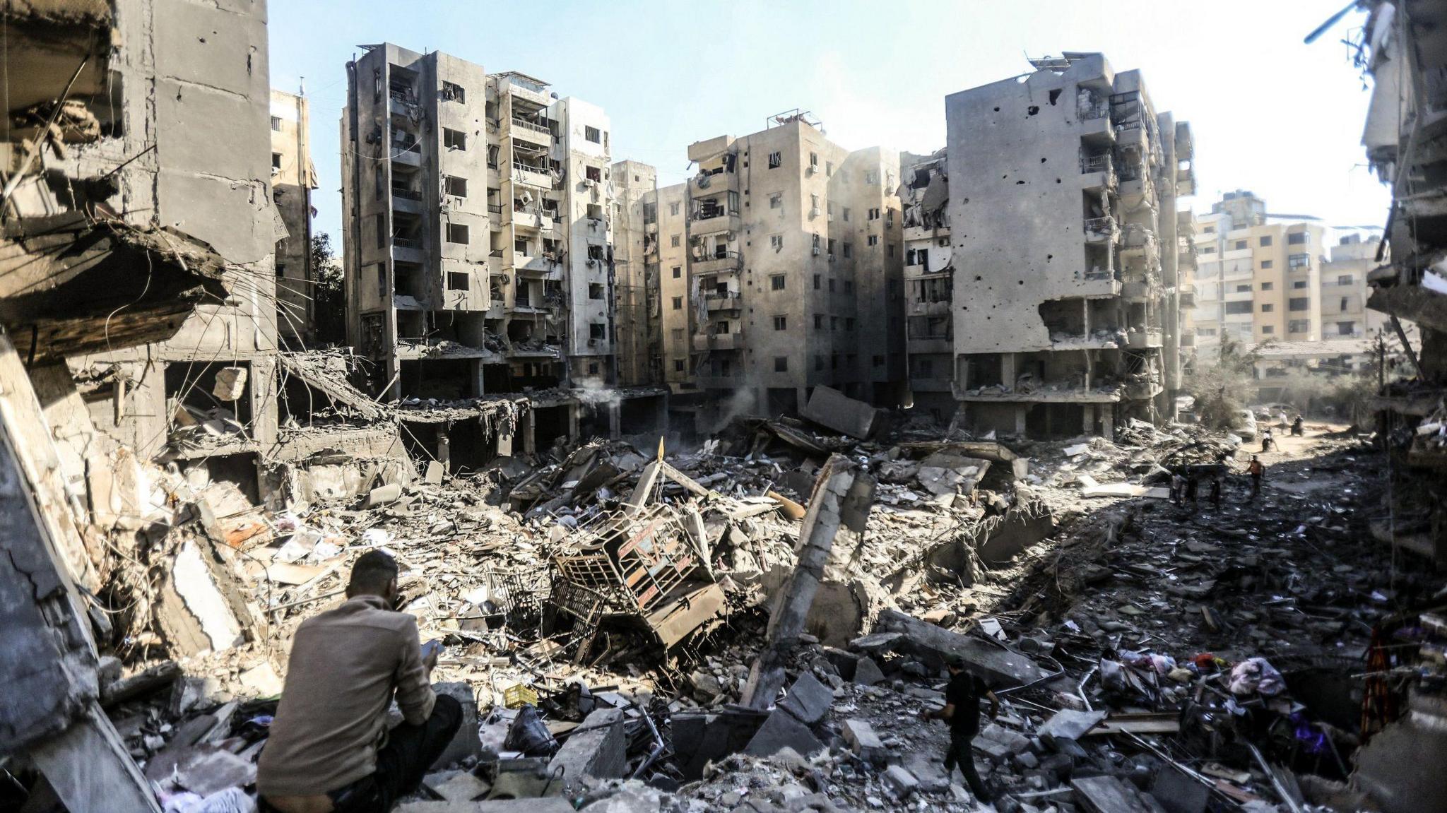 A man sits looking out to rubble