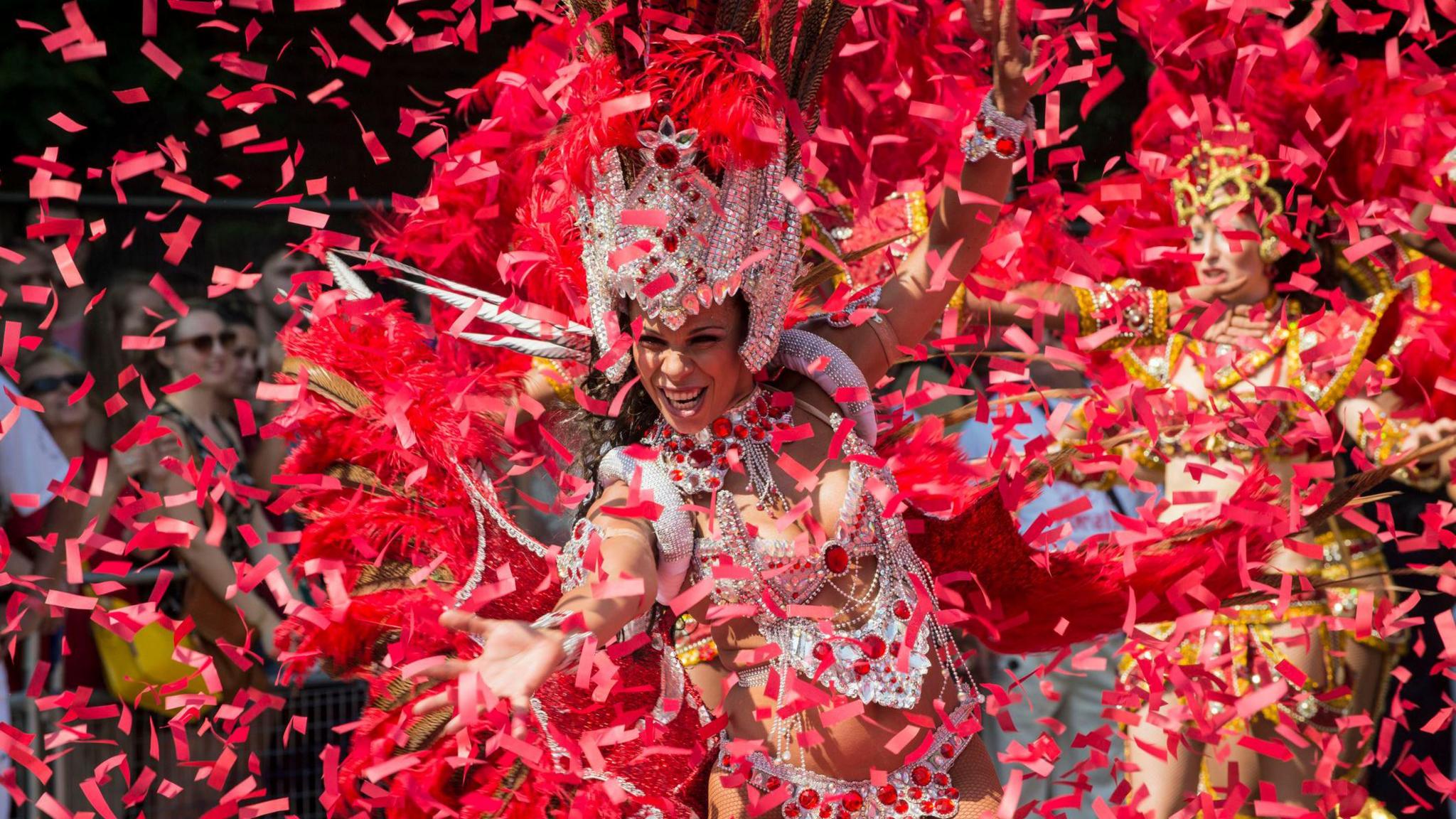 Dancer in elaborate, brightly coloured feathered costume takes part in a vibrant street parade during Notting Hill Carnival.