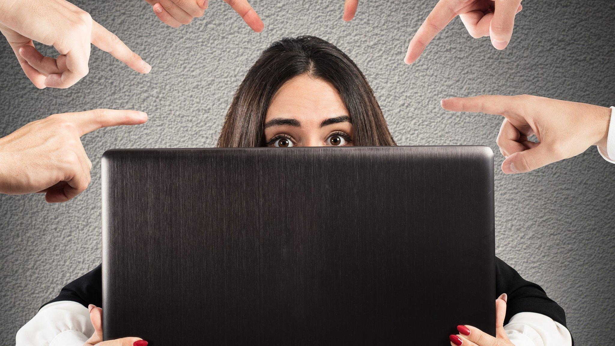 Woman hiding behind laptop