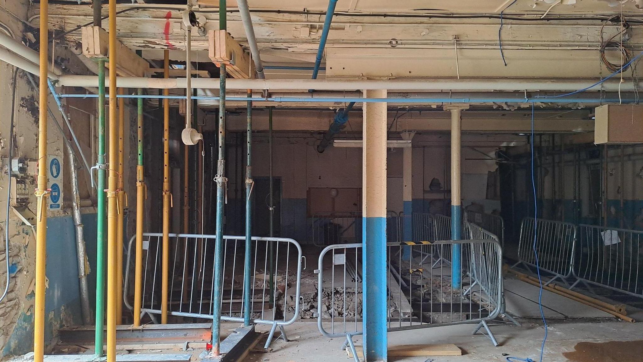 The interior of a mill building propped up by metal bars and with metal railings inside looking dilapidated