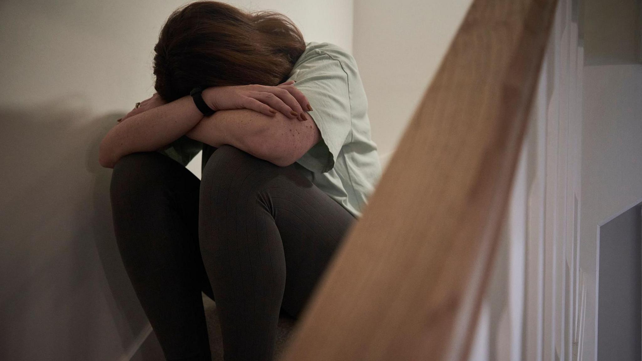 Library photo of a woman sat at the top of some stairs, head in hands. Her face can't be seen