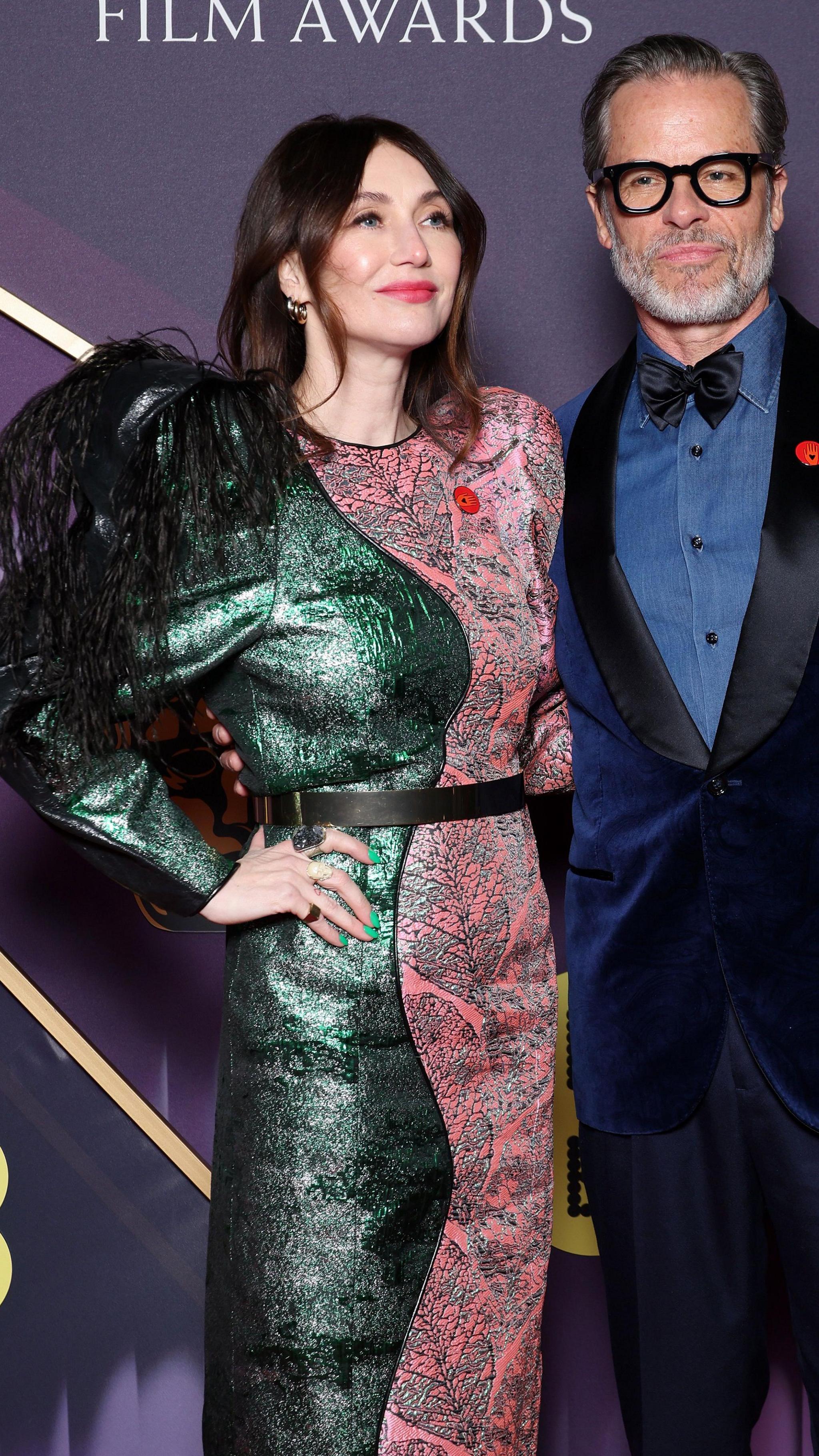 Carice van Houten and Guy Pearce; she is in a green and pink dress and he is in a blue, velvet suit