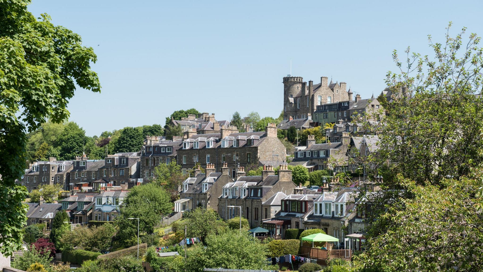 A general view of Selkirk. A collection of stone house built in a series of terraces on the side of a hill. They are surrounded by green trees.