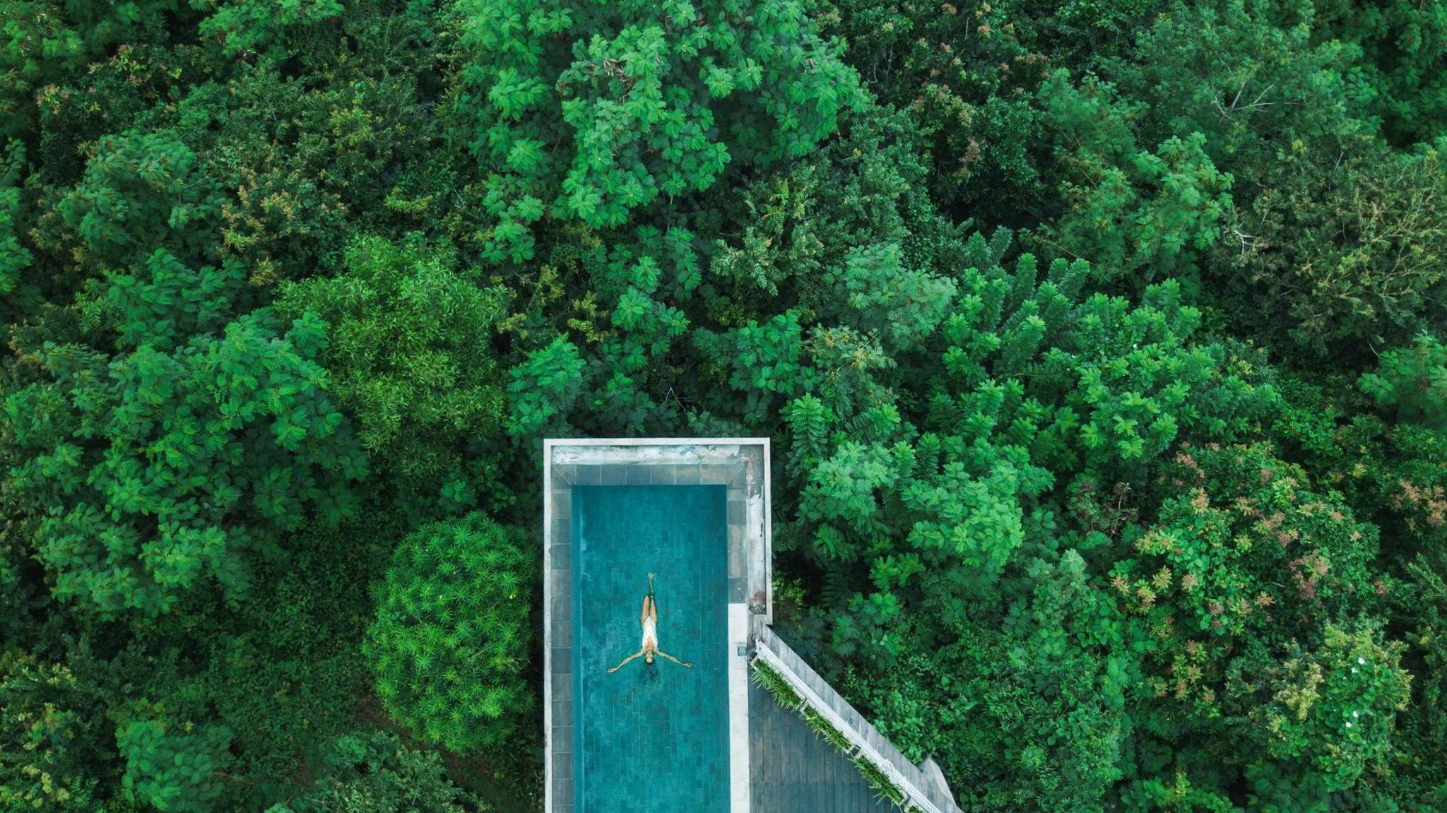 Drone aerial shot of woman relaxing in awesome infinity swimming pool in Bali. 