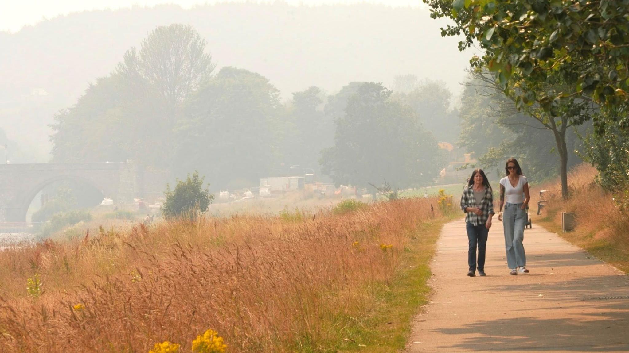 Two people walking along a path. The sky is hazy