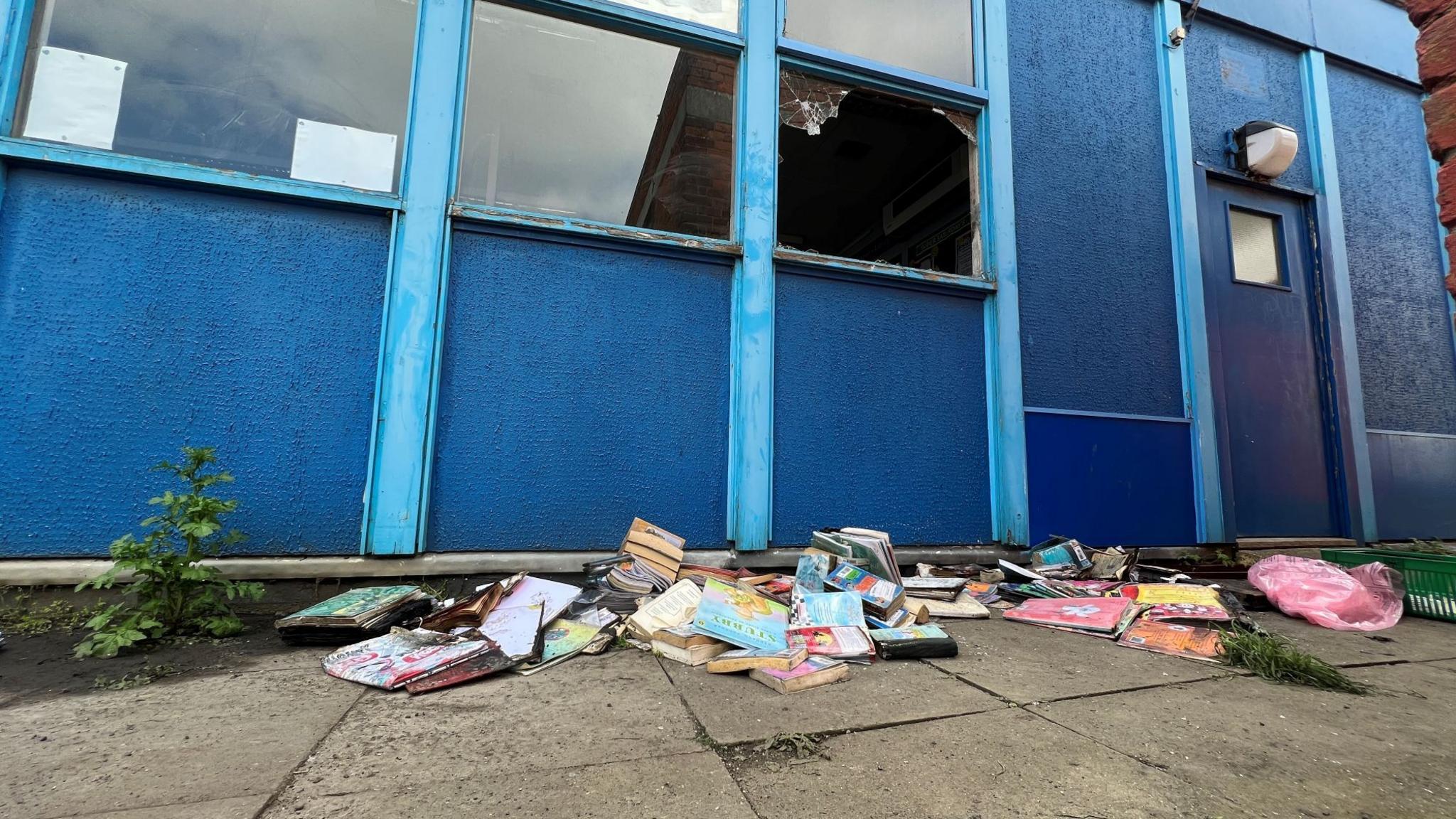 Books piled up on the floor below a broken window