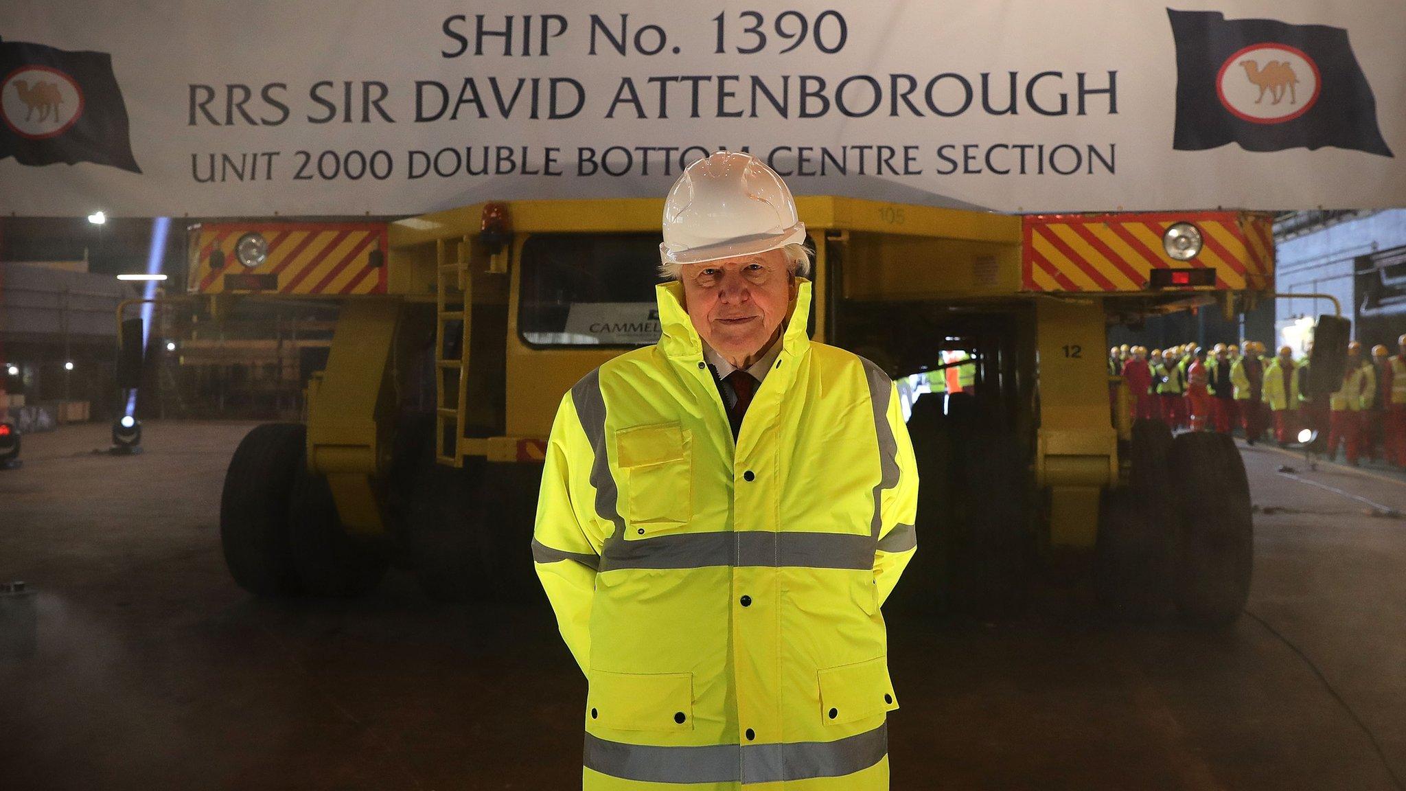 Sir David Attenborough stands in front of a sign announcing the polar research ship named after him.