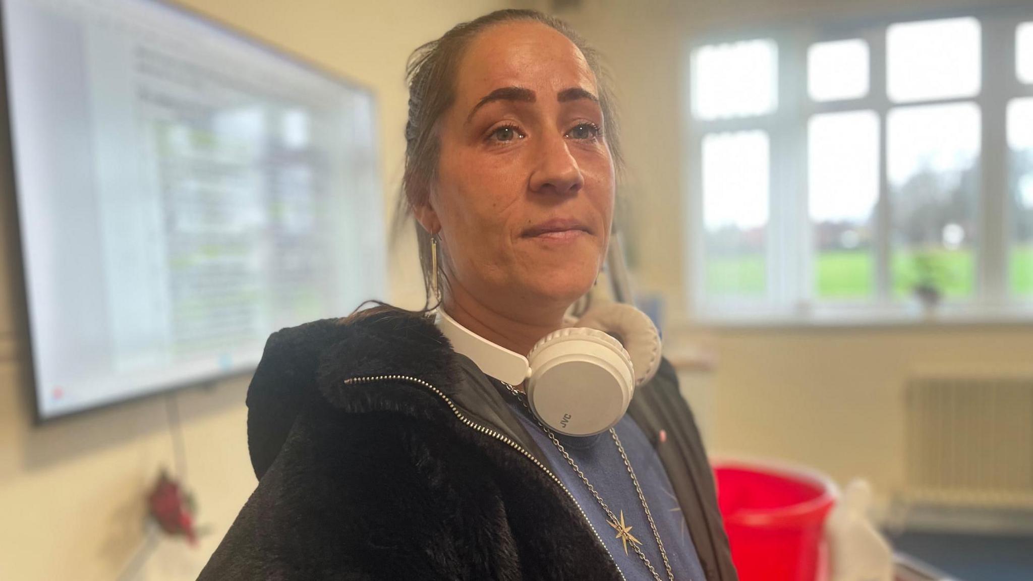 A woman with white headphones around her neck smiles shyly at the camera