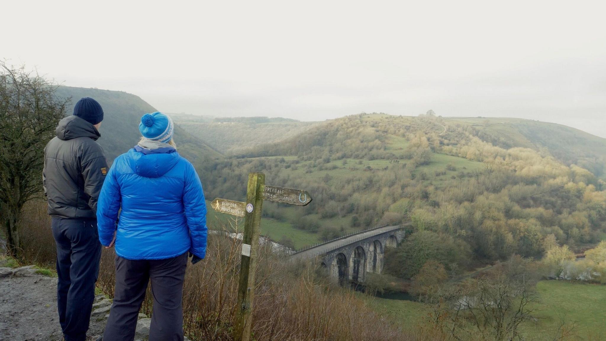 Two people with their back to the camera at the Monsal Trail enjoying a view of the Peak District.