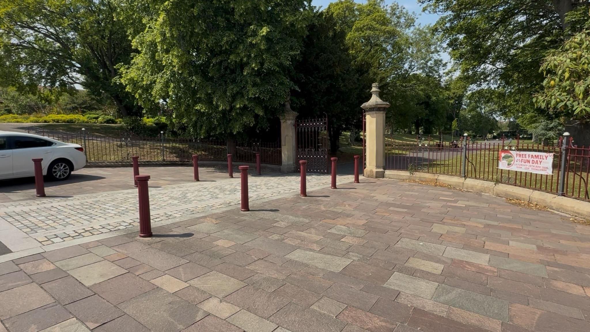 The stone and metal entrance gates of Barnes Park. A banner promoting an upcoming family fun day is hanging on the red fence.
