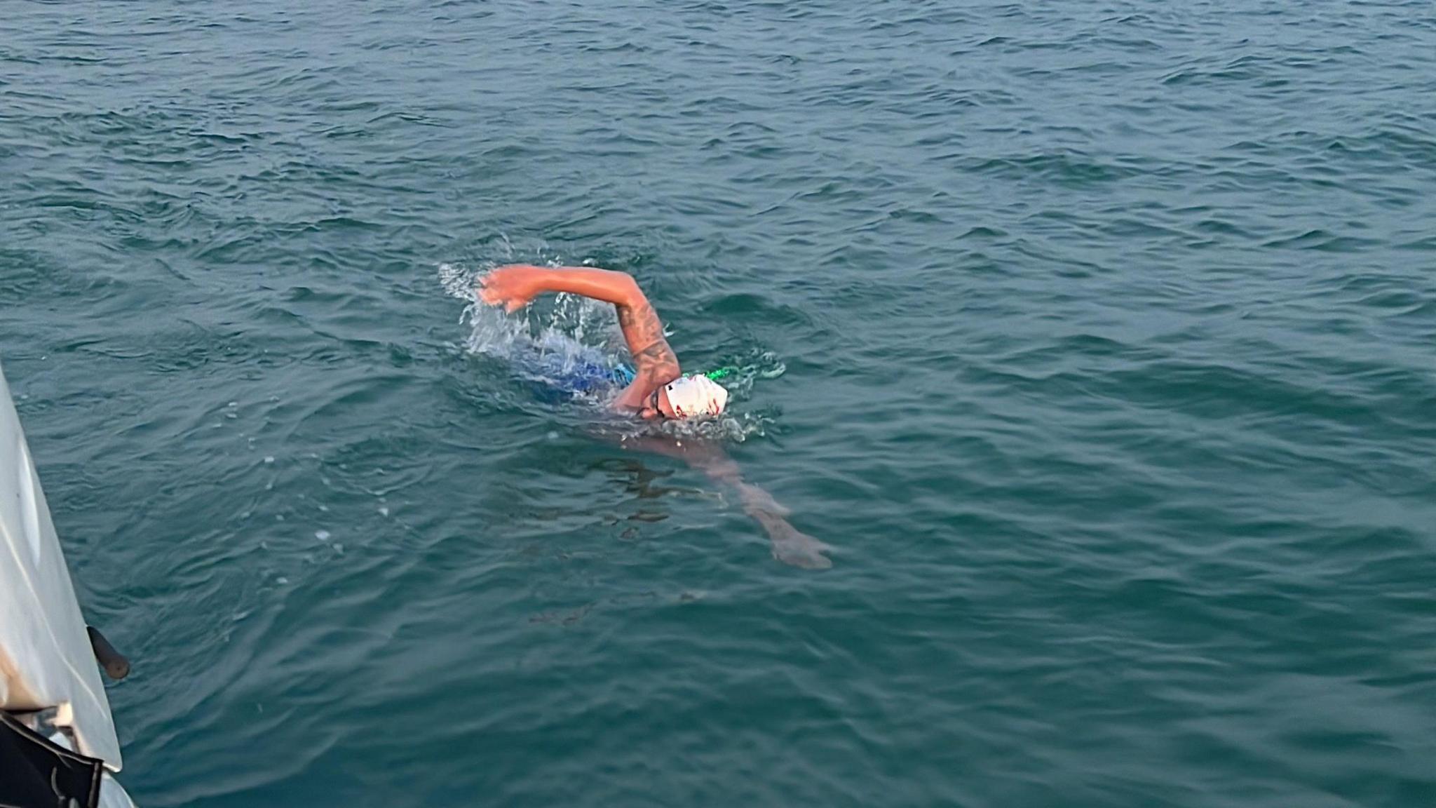 Neil Gilson swimming in the water. He is moving in the water and is wearing a white swimming cap.