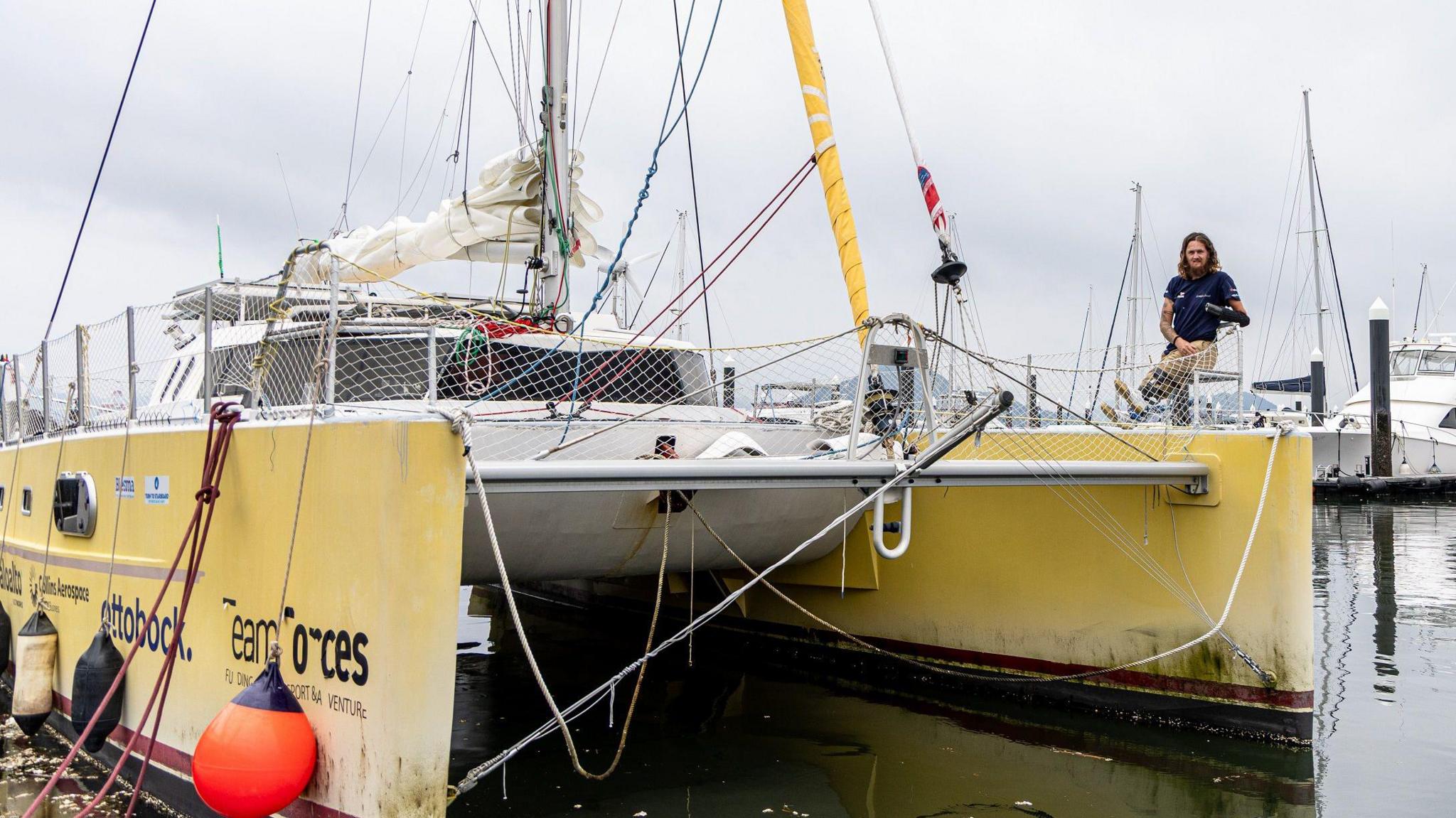 A yellow catamaran boat with 'Team Forces' written on the side. A man leans off the right side.