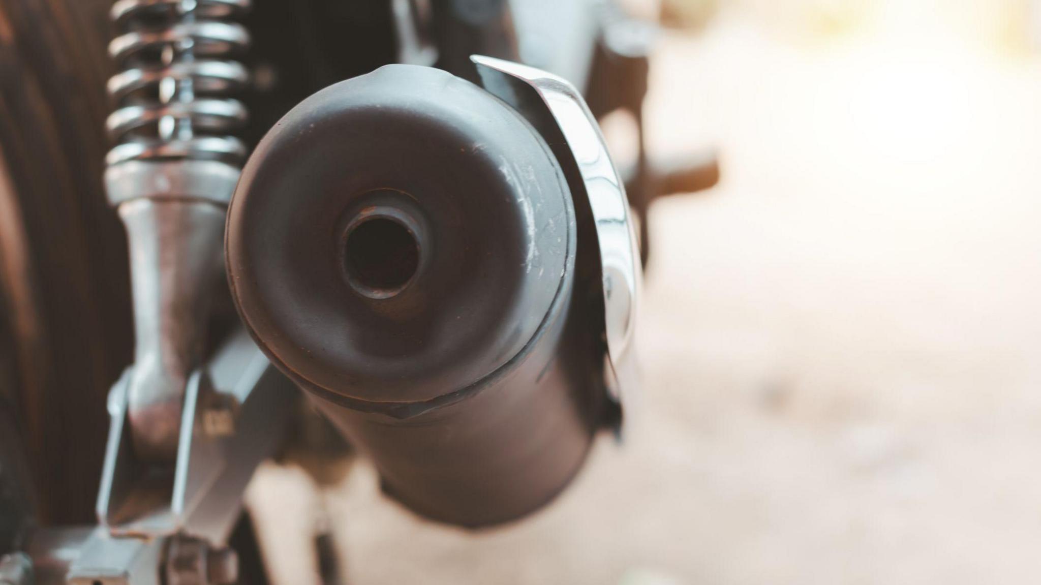 A large motorbike exhaust. The exhaust is in focus while the rest of the image is blurry.