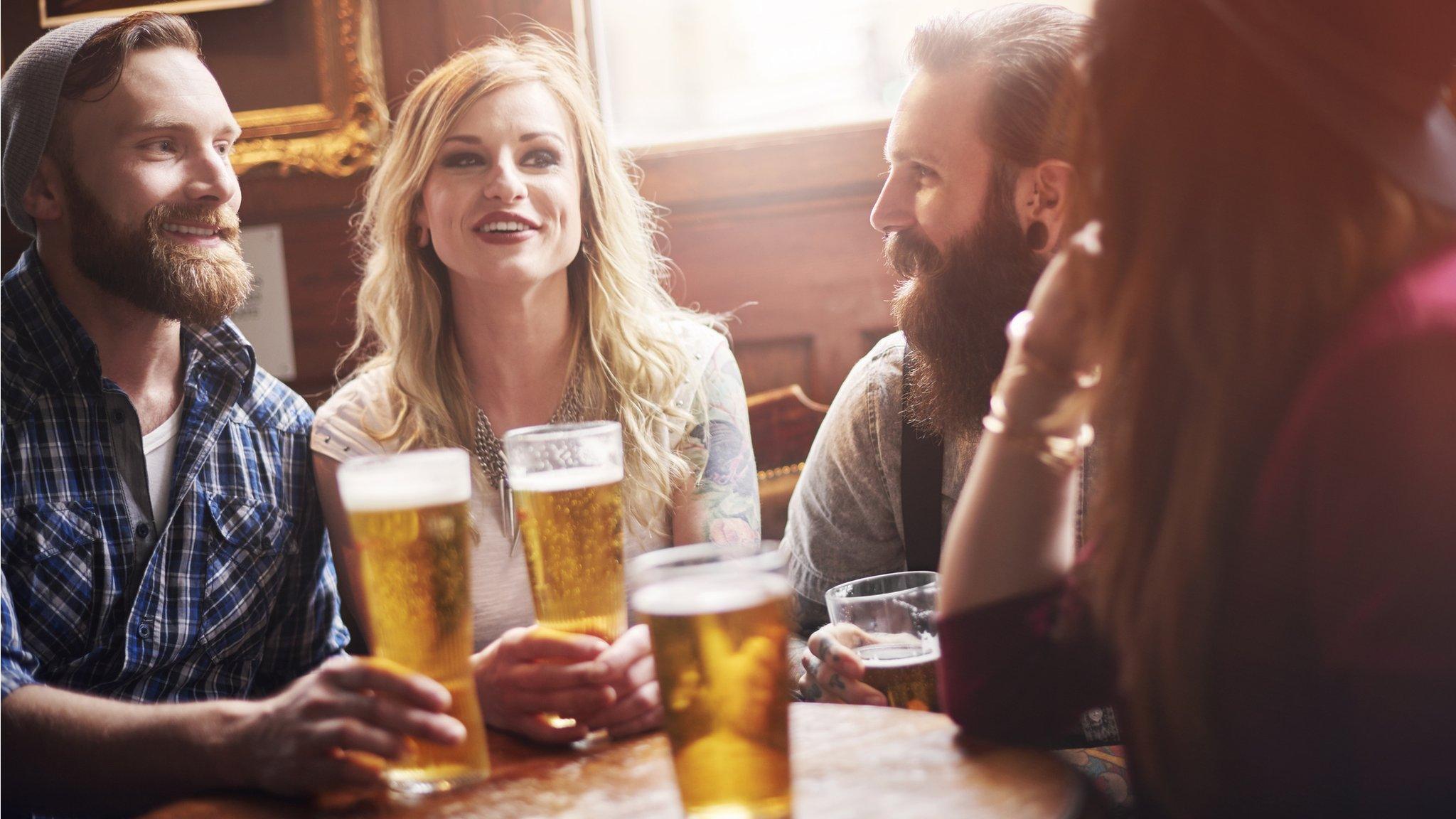 Four friends sitting at a pub table drinking a pint of beer.