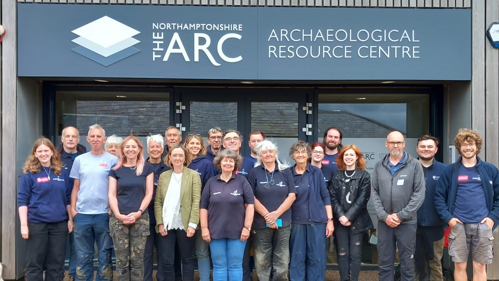 A big group of people stand in front of a building with a sign reading "Archaeological Resource Centre"