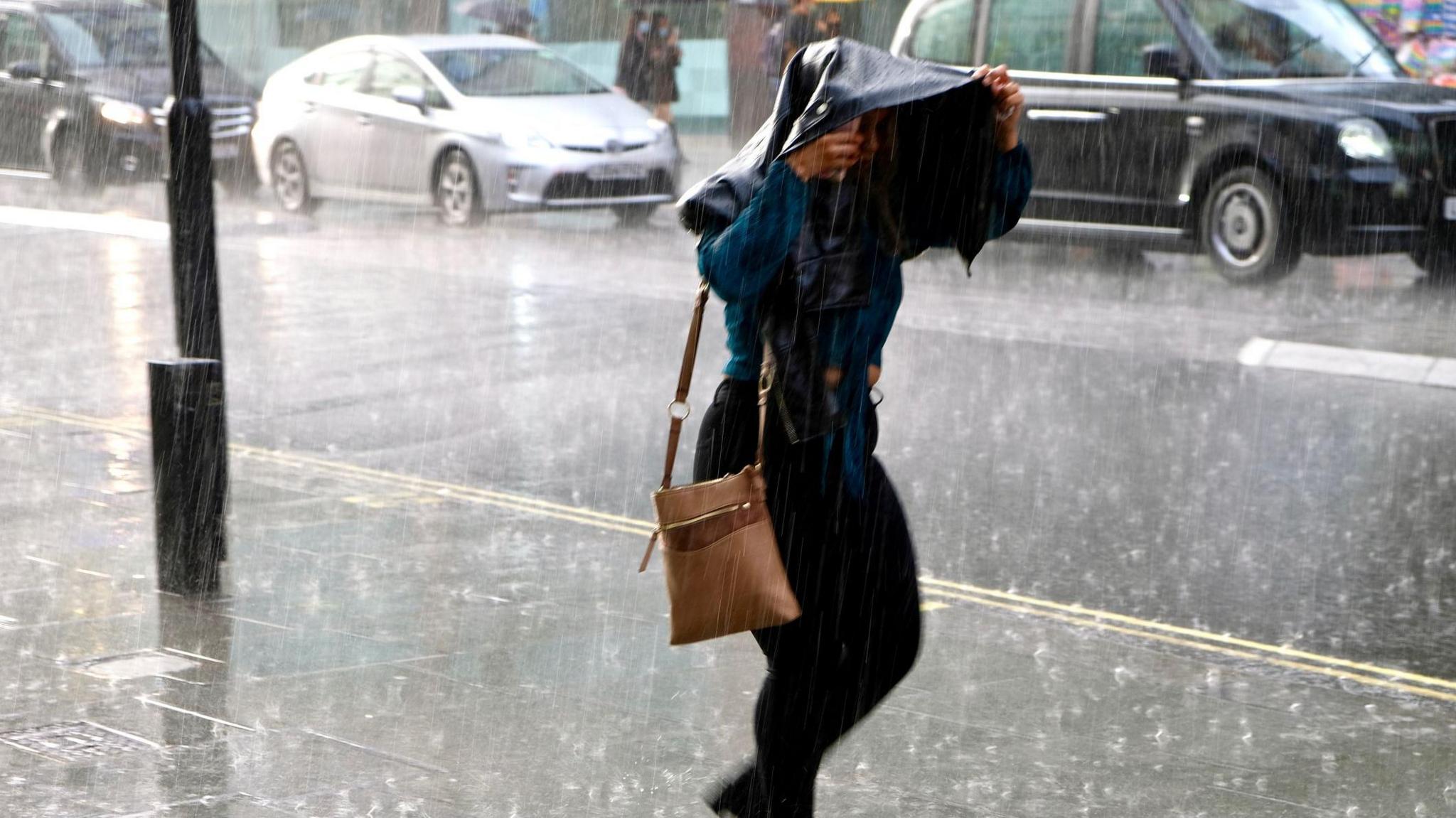 Woman walking in heavy rain holding a jacket over her head.