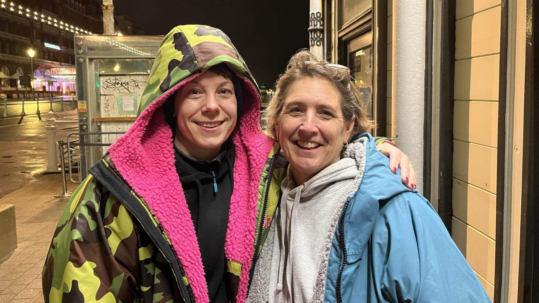 Comedian Suzi Ruffell (left - with a camouflage coat and a pink inside) and Fabia Bates (right - a woman with blonde hair, a grey hoodie and a blue coat)