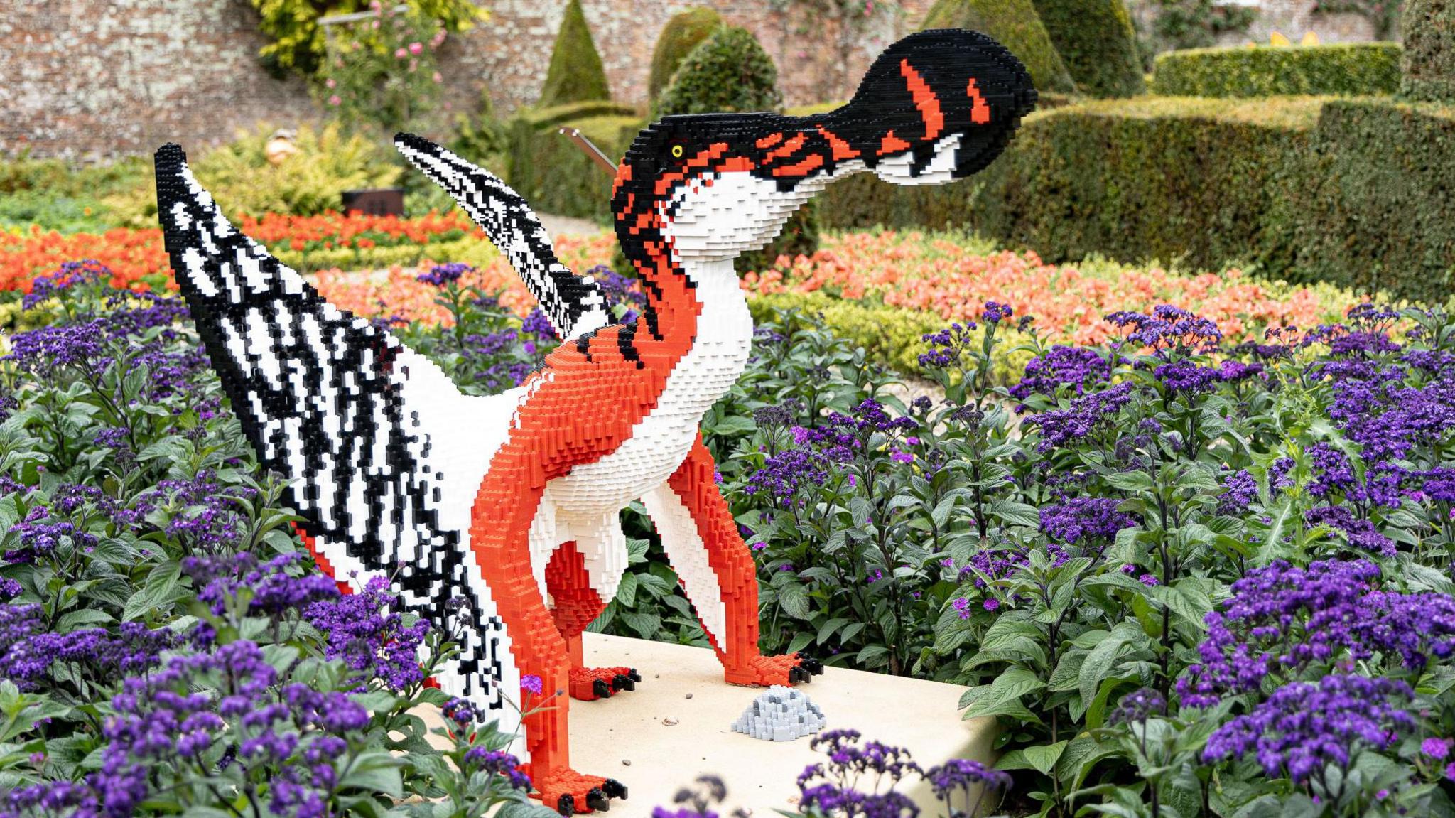 A Lego model dinosaur, made from red, black and white bricks, sits in a bed of purple flowers at Sewerby Hall