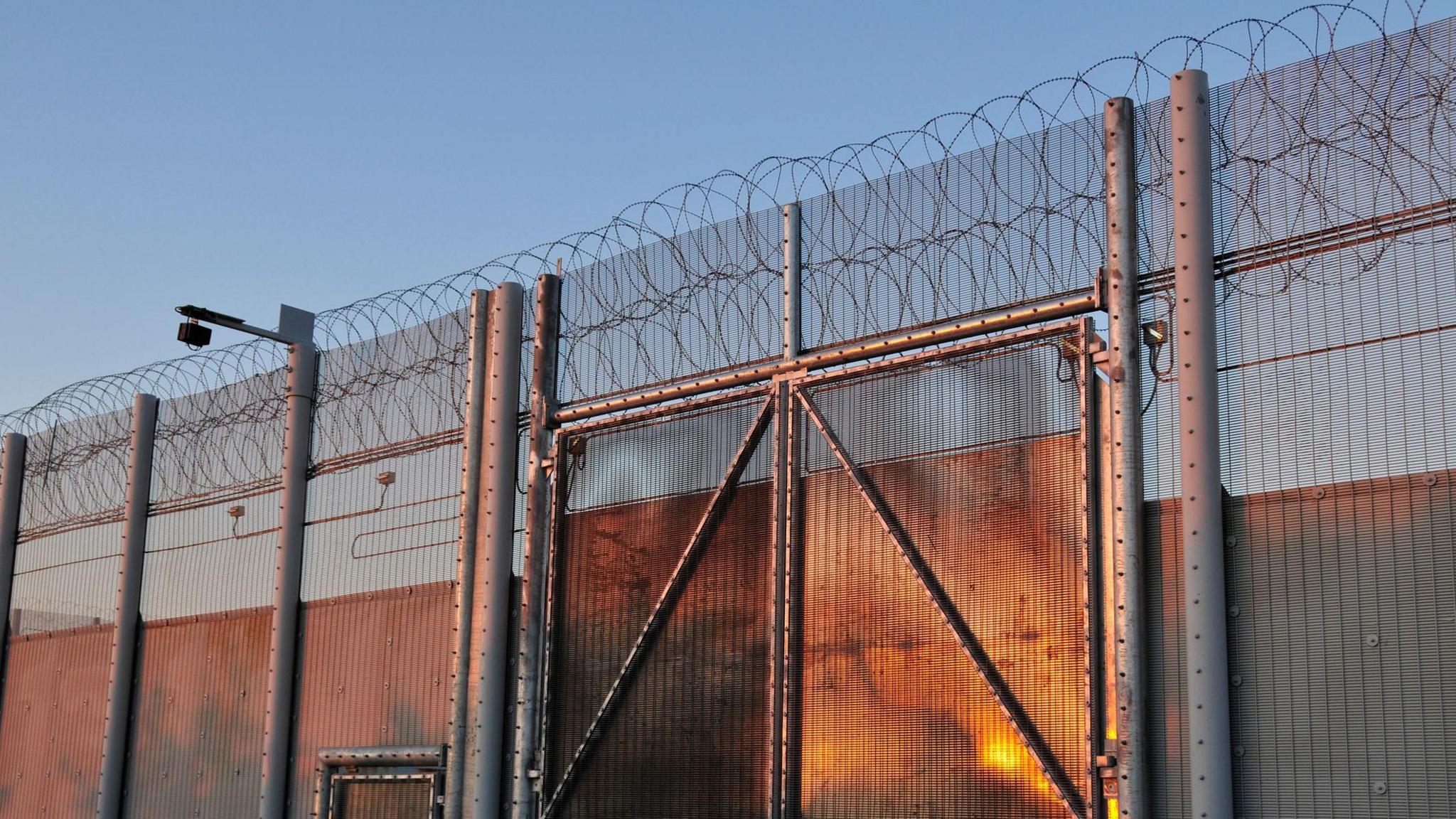 A prisoner wall with barbed wire on top, in evening light.