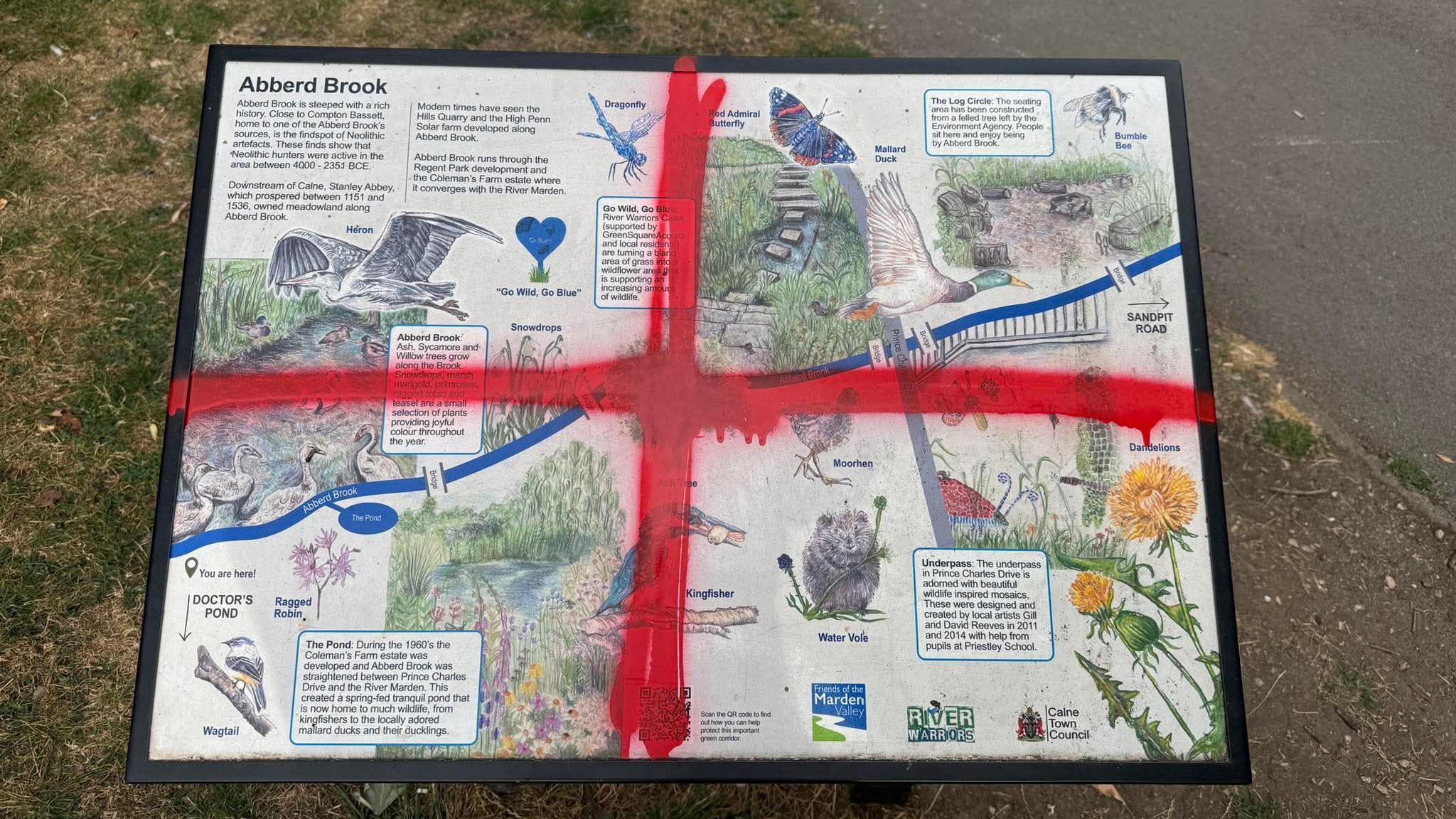 A red cross painted onto a board for Abberd Brook, showing paintings and descriptions of local wildlife.