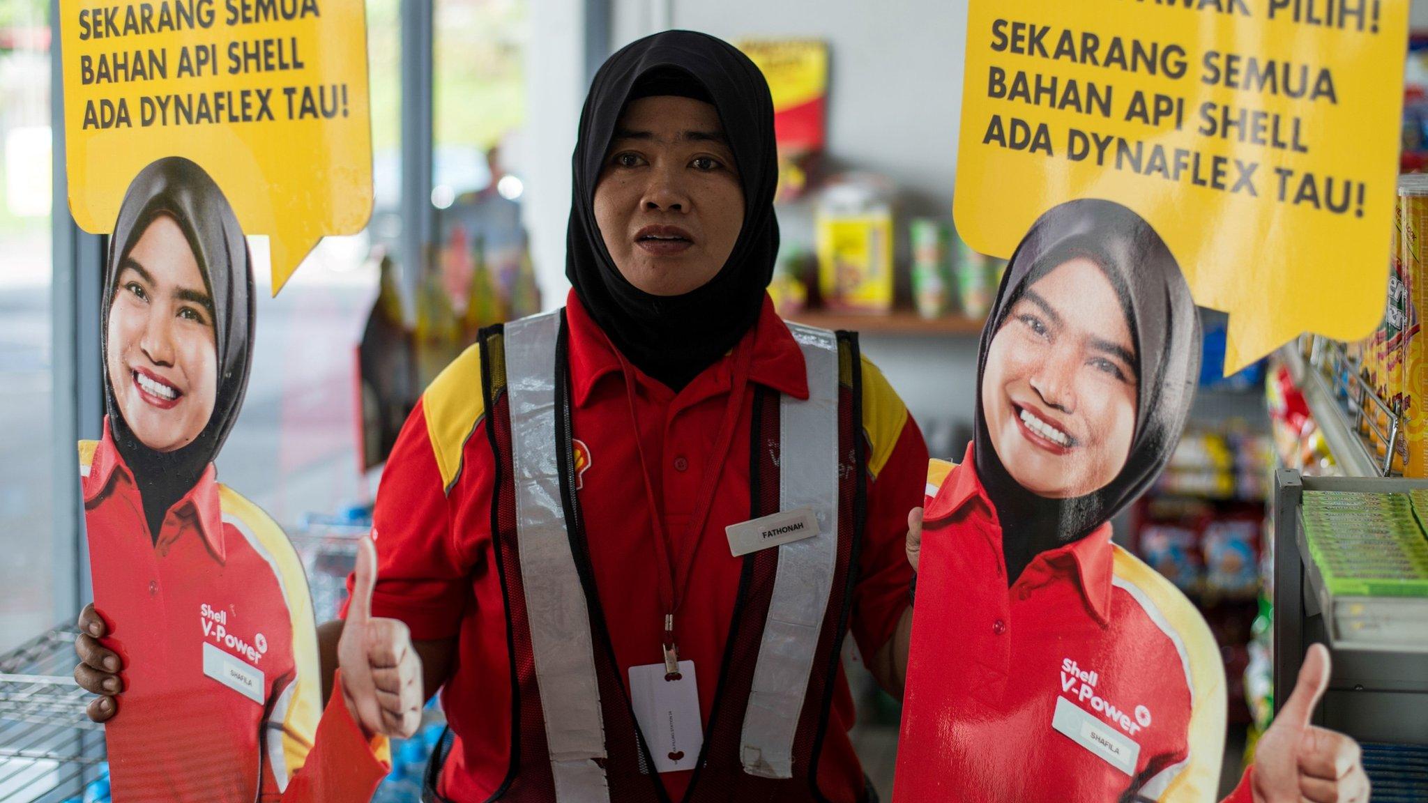 A Shell petrol station employee holds up life-sized cutouts depicting a female staff member, pictured in uniform with a black Muslim headscarf and placed beside individual self-serve petrol pumps as part of a promotional campaign, as they were pulled from display at a Shell station in Bentong, some 70 kms north of Kuala Lumpur in nearby Pahang state on July 4, 2017