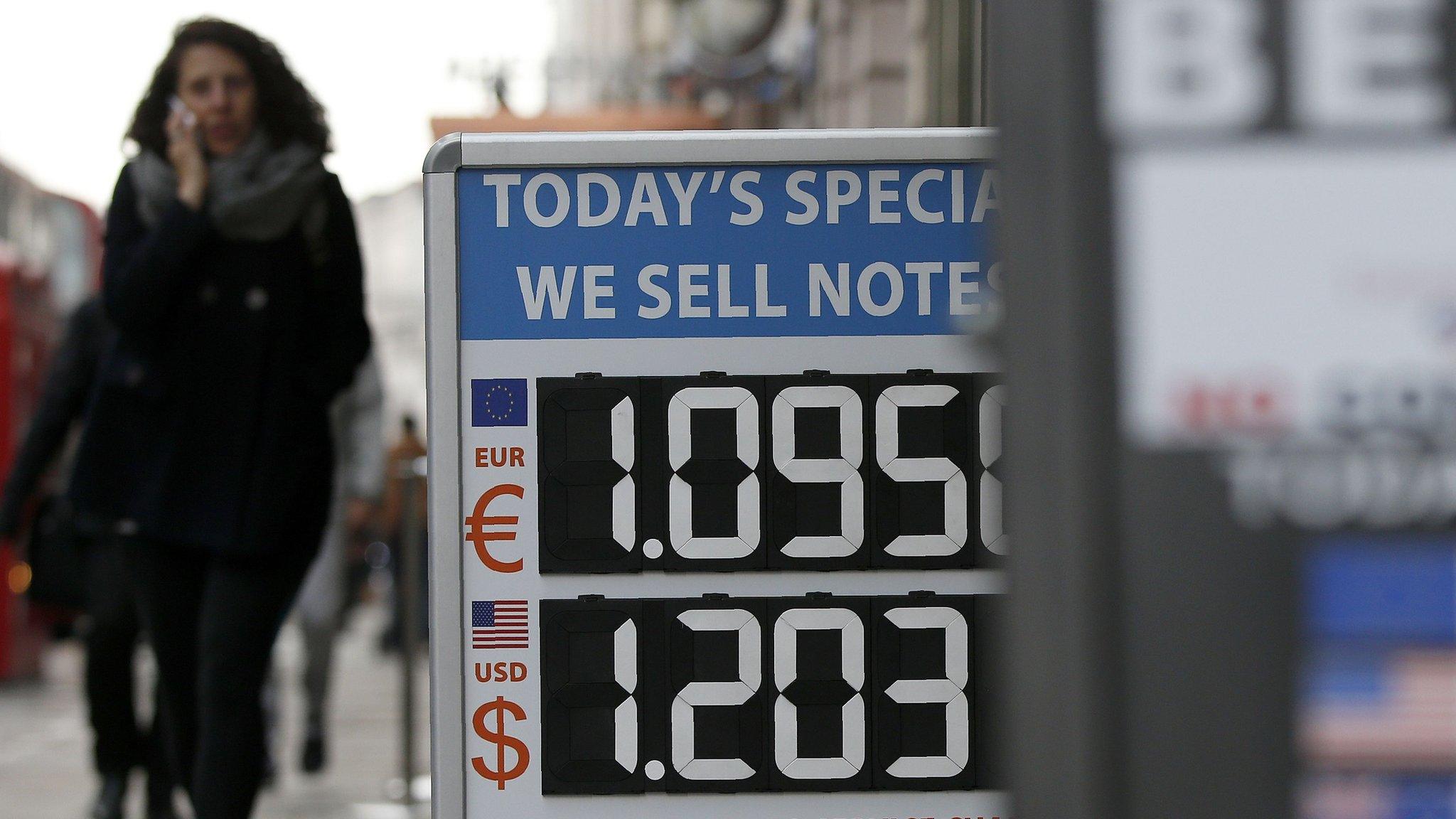 A woman walks past a board displaying the price of Euro and US dollars against British pound