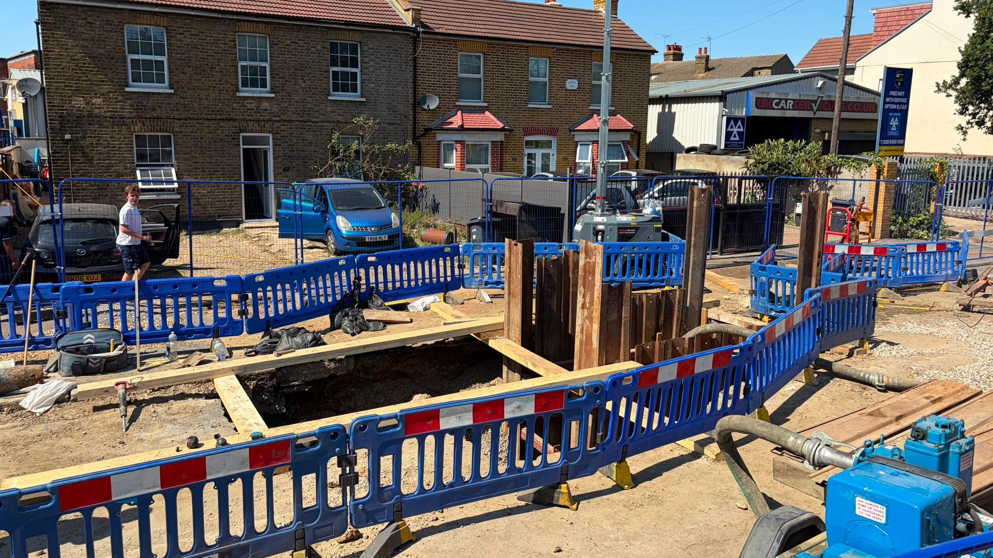 Blue roadworks fencing surrounding a large pile in the middle of a residential street.