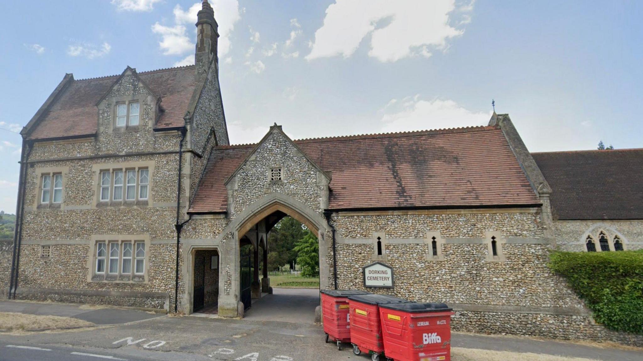 The Victorian Gothic entrance to Dorking Cemetery, featuring a chapel, with some red wheelie bins standing outside the main gate.