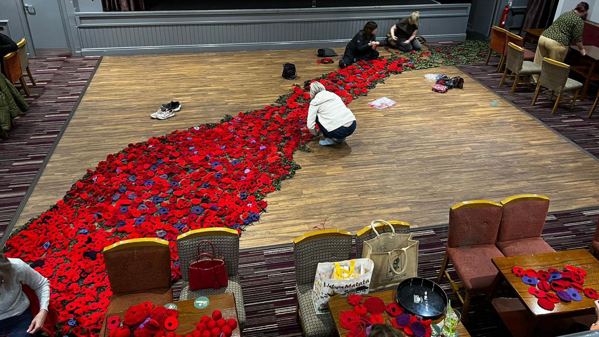 A group of people in a large hall working on the poppy cascade