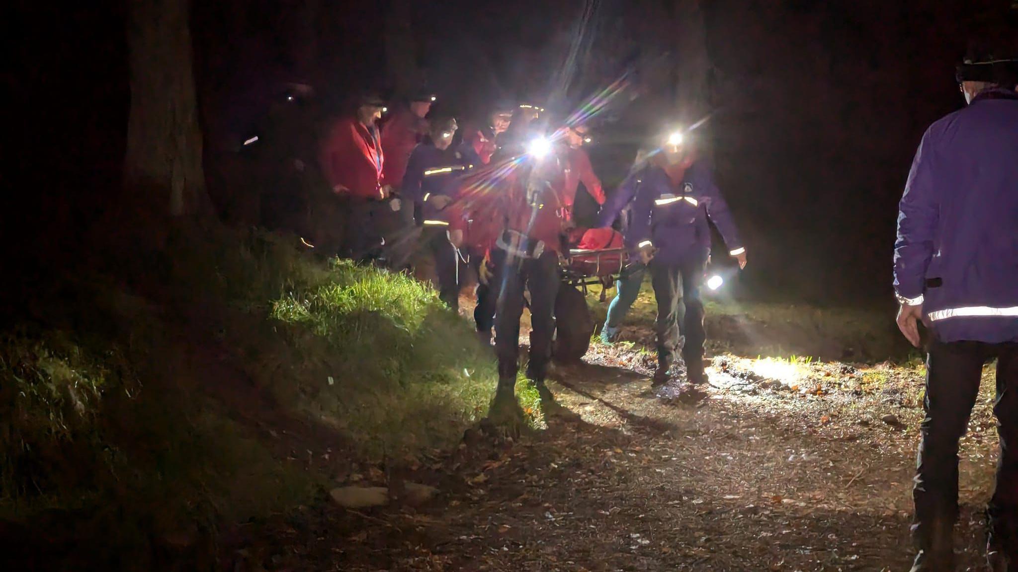 A mountain rescue team with head torches and other lighting take someone to safety on a stretcher in the dark