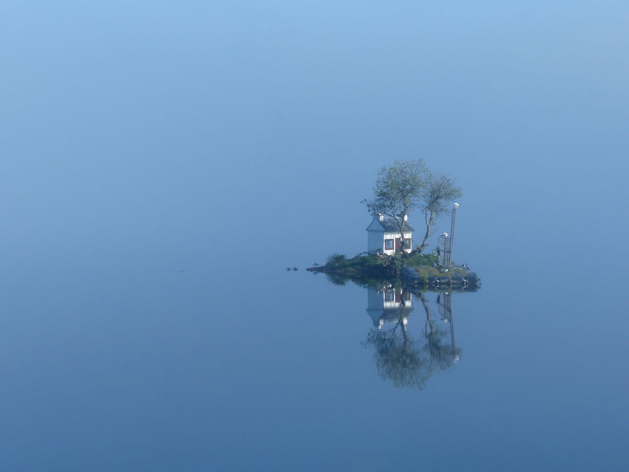 Blue sky and water fading into each other with a small island with a small white house and tree