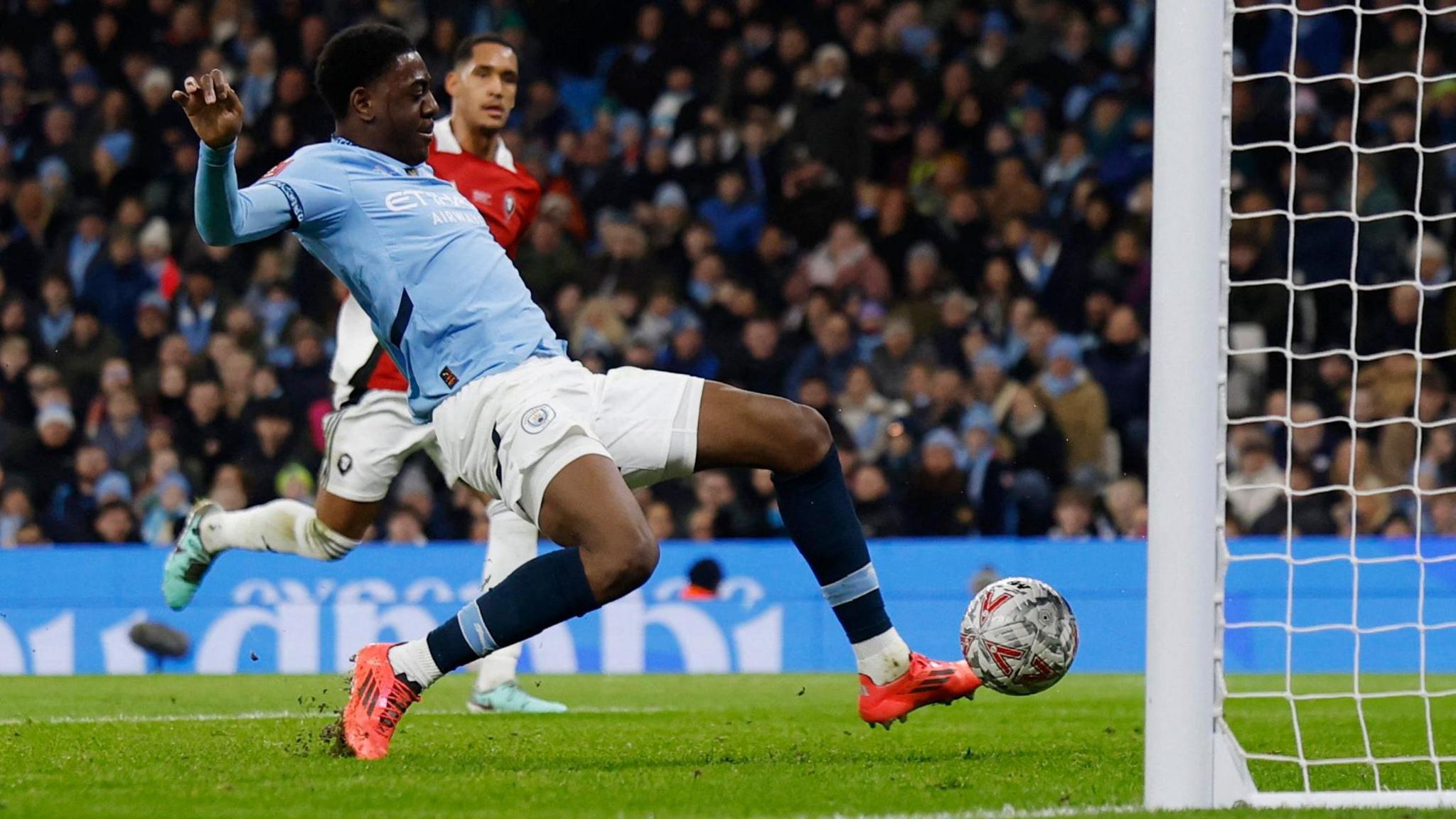 Divin Mubama stretches to touch the ball home to score for Manchester City