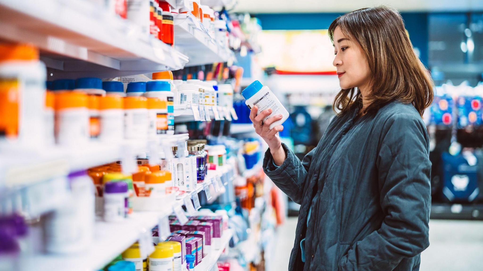 A woman in a pharmacy looking at a range of medications on the shelves