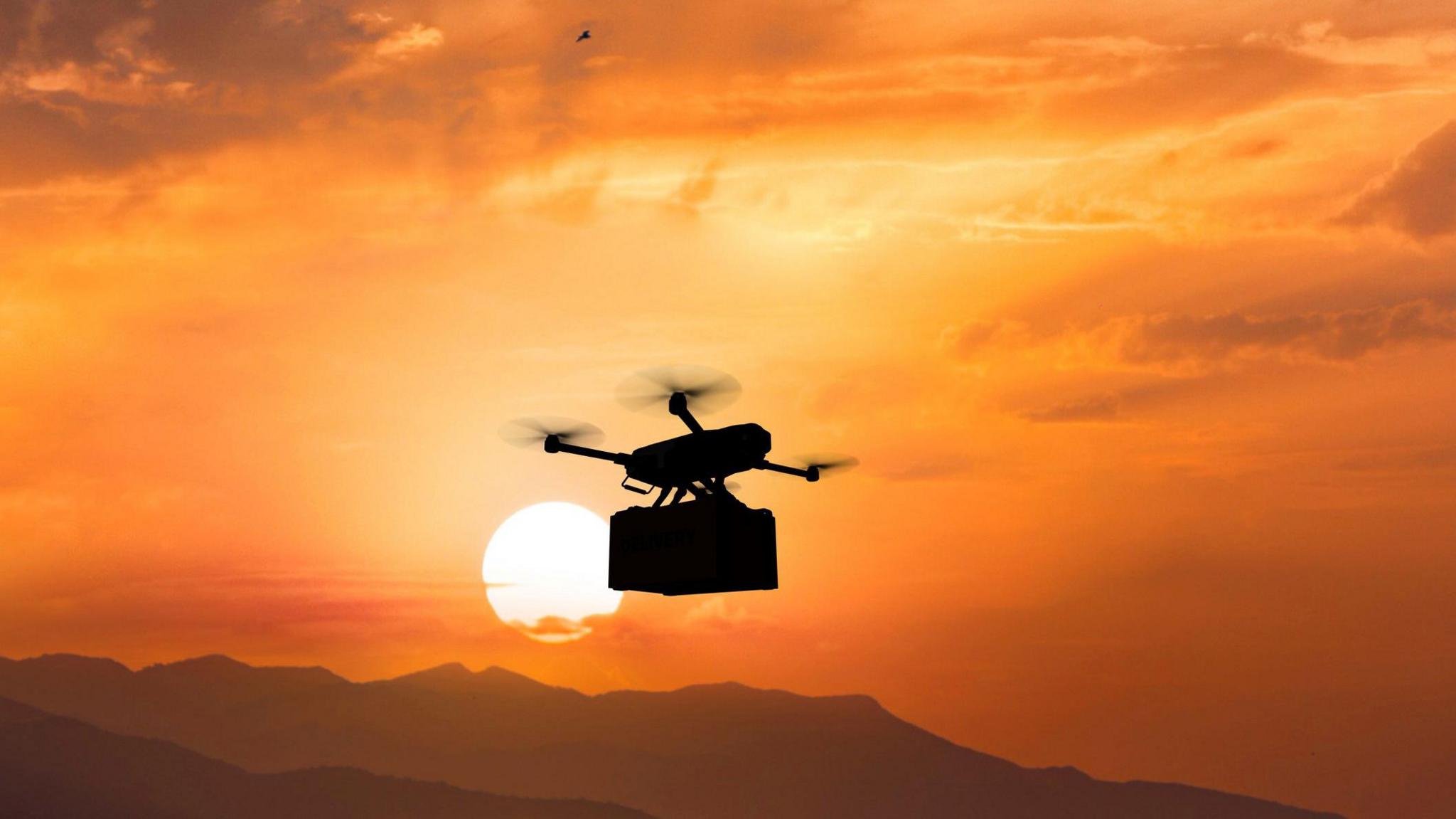 Dròna a' giùlain stuth san adhar le beanntan air fàire agus a' ghrian a' dèarrsadh