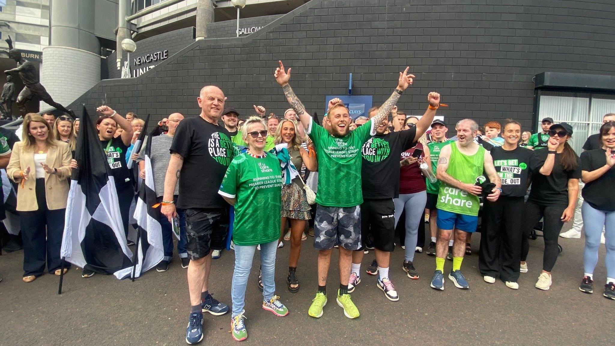 Matthew Smith cheering outside St James' Park having completed his run. He is standing next to his mother and father and a crowd of supporters are behind him.