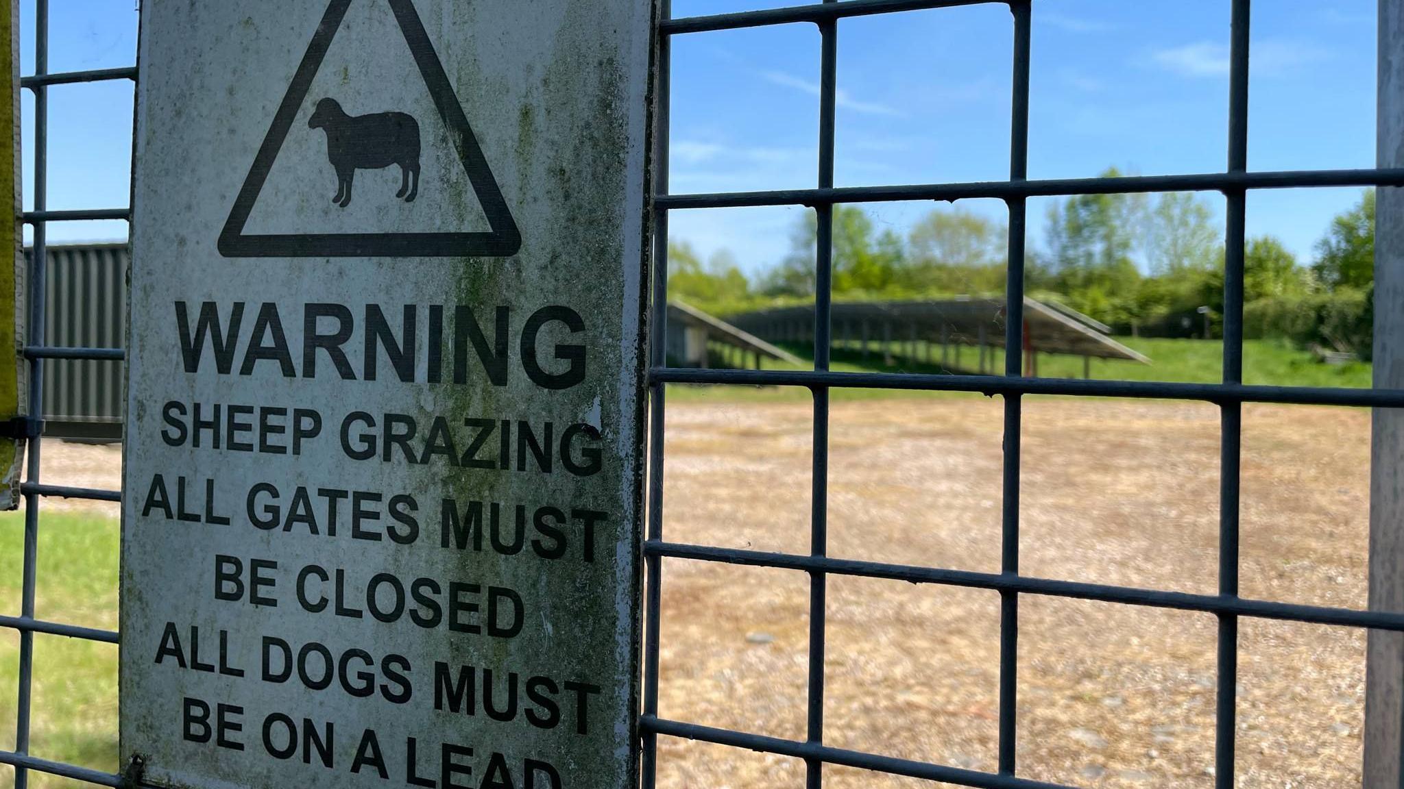 A sign about grazing sheep on the fence of a solar farm