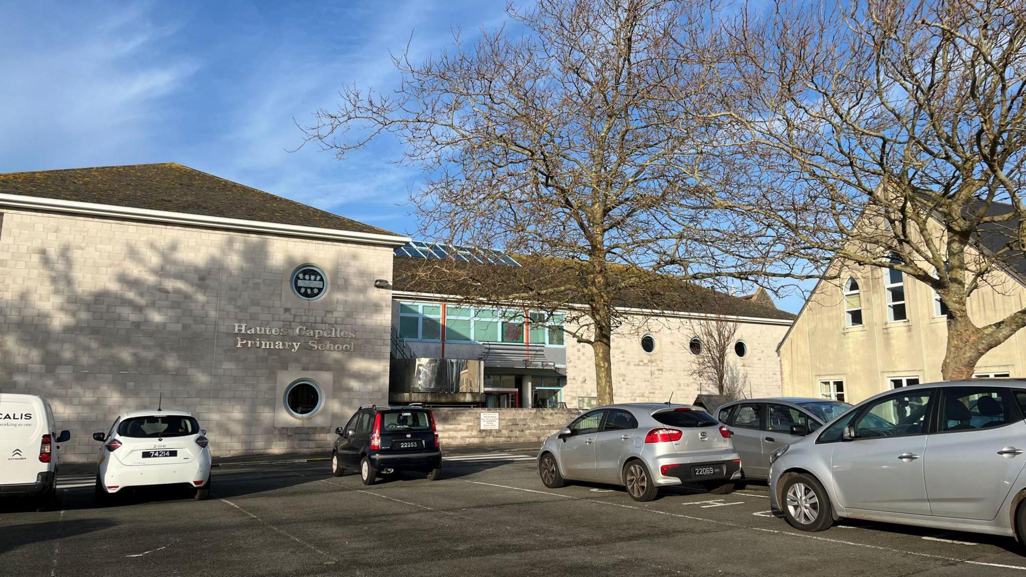 Hautes Capelles Primary School. A modern school building with trees and cars in the carpark.