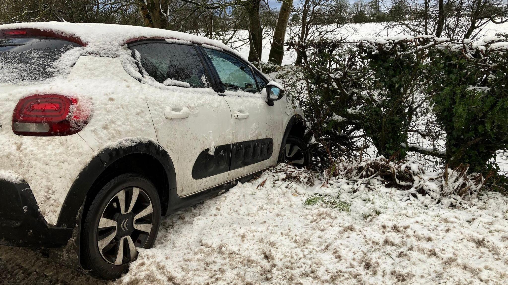 A white car faces into a hedge at Claudy in Co Derry. Snow can be seen all around.