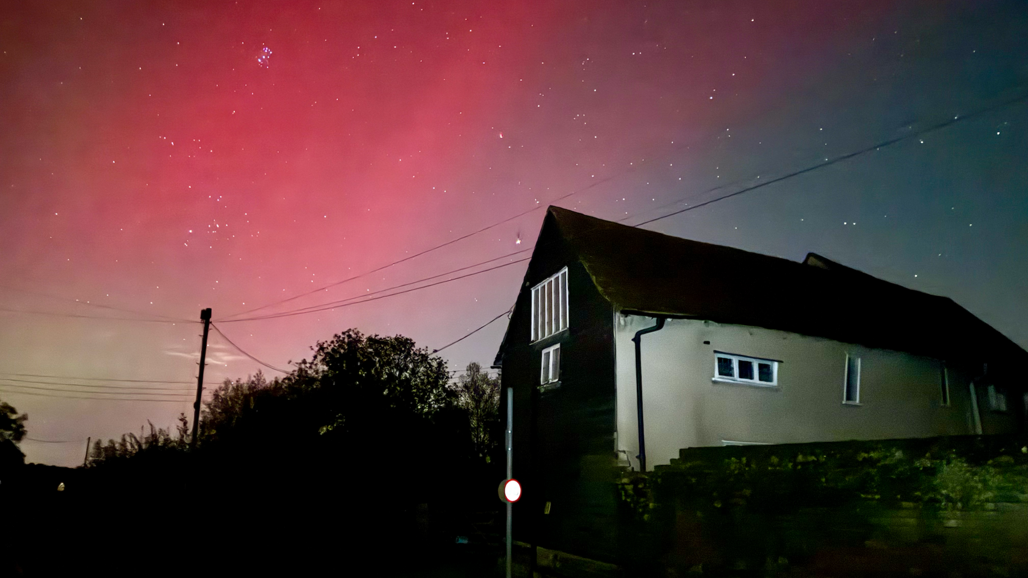 An old barn which has been turned into the Dark Sky Discovery Centre against a a starry night sky with vivid red northern lights.