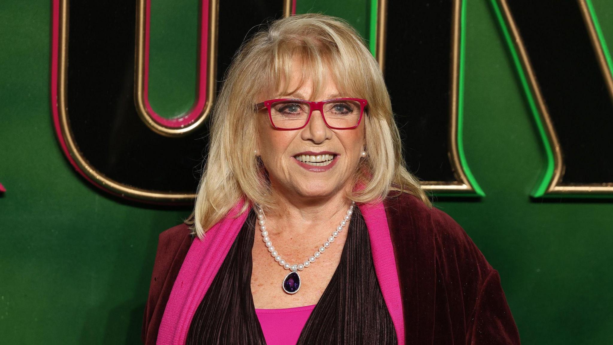 Elaine Paige smiling on the red carpet, and wearing a pair of red glasses