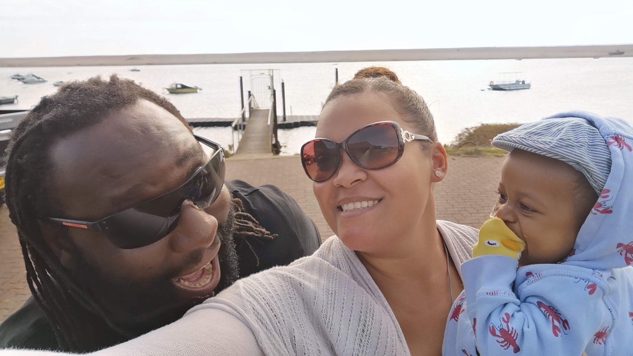 A man and woman wearing sunglasses with a baby in a hat.
