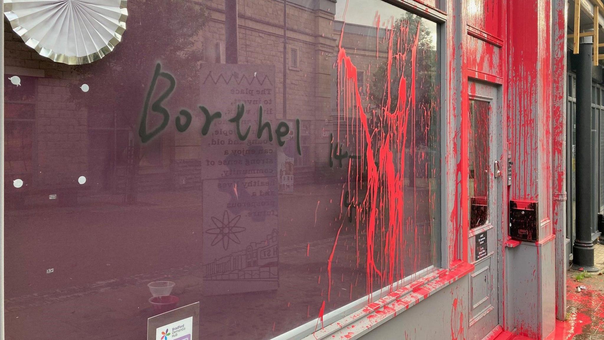 The word 'borthel' in black paint sprayed on a window which also has red paint running down it.  