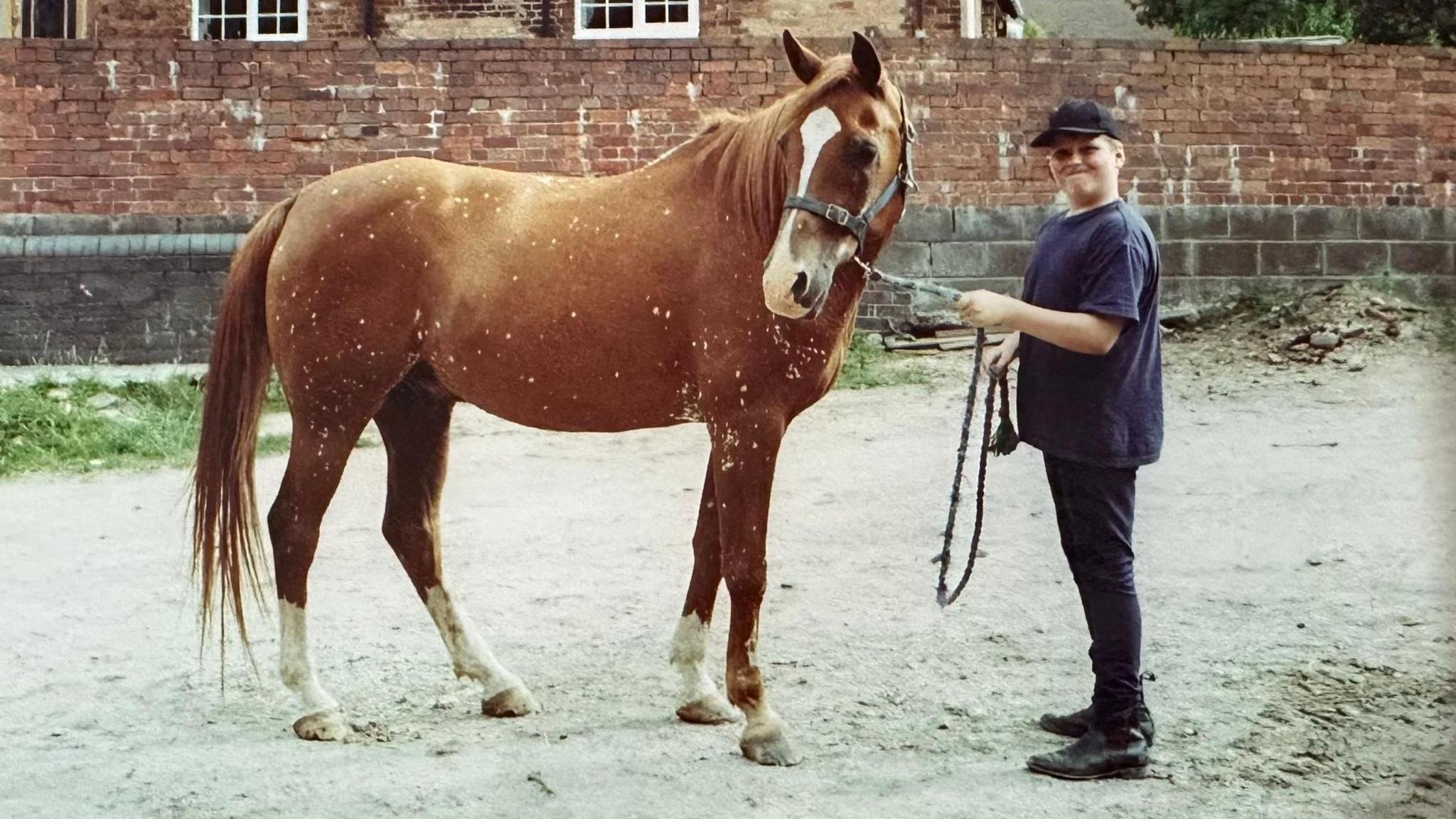 Young Jordan stands in front of a horse, holding it by its reins.