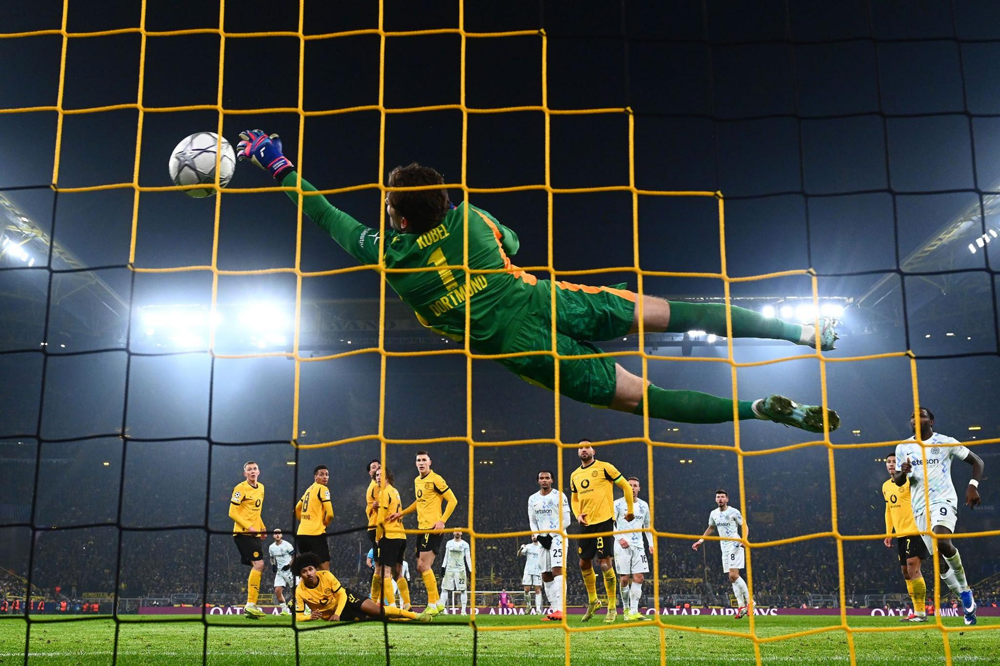 A goalkeeper in a green kit dives fully outstretched toward the top corner of the goal, beaten by Inter Milan's Federico Dimarco in the UEFA Champions League 2025/26 League match against Borussia Dortmund at Signal Iduna Park. The photo is taken from behind the goal. 