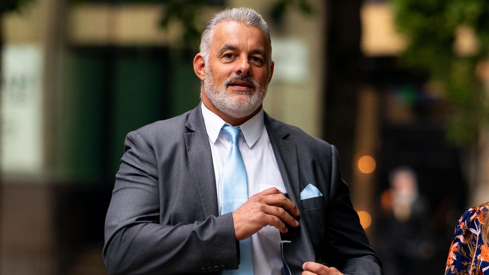 PC Lee Willis, a white man with a white beard and white, short hair, in a grey suit with a light blue tie and pocket square.