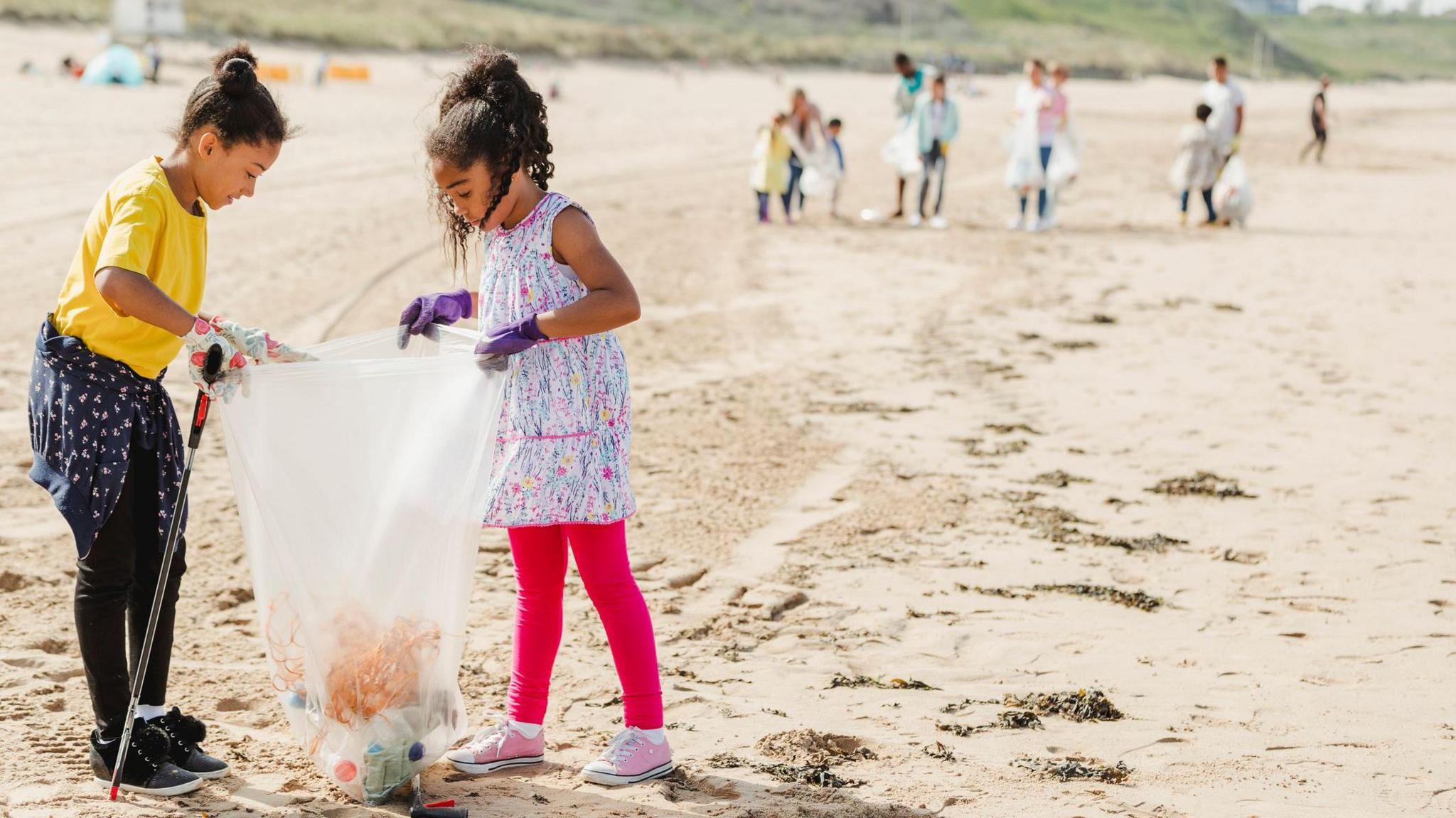 Two girls at a beach clean up collecting rubbish. 