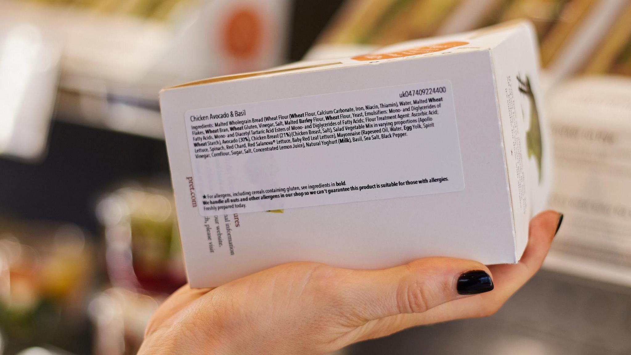 A woman's hand holds a food label on a sandwich.