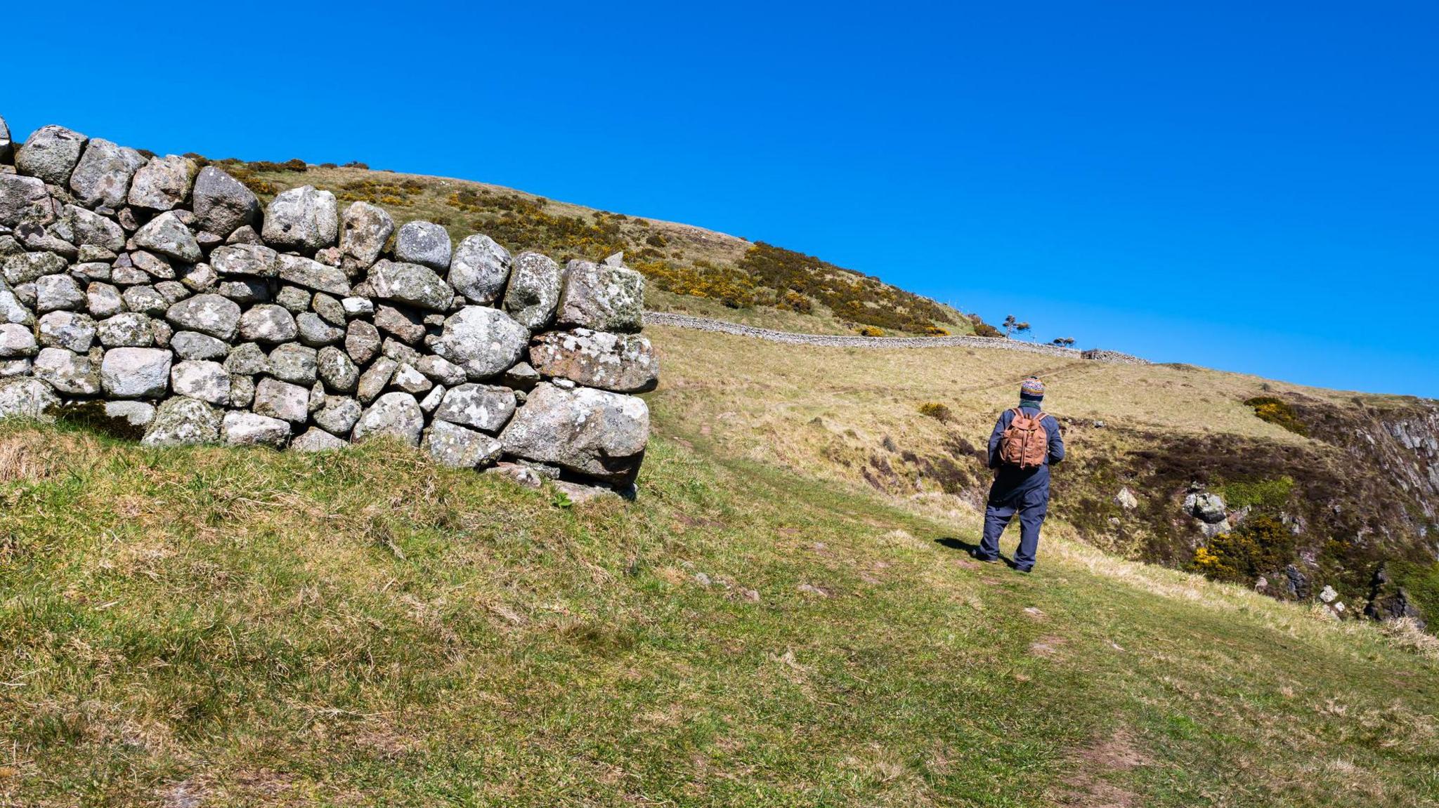 A man with a backpack standing alone in the countryside on a hill.